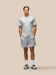 A man modeling a light gray heathered athletic t-shirt and matching shorts against a solid beige background.