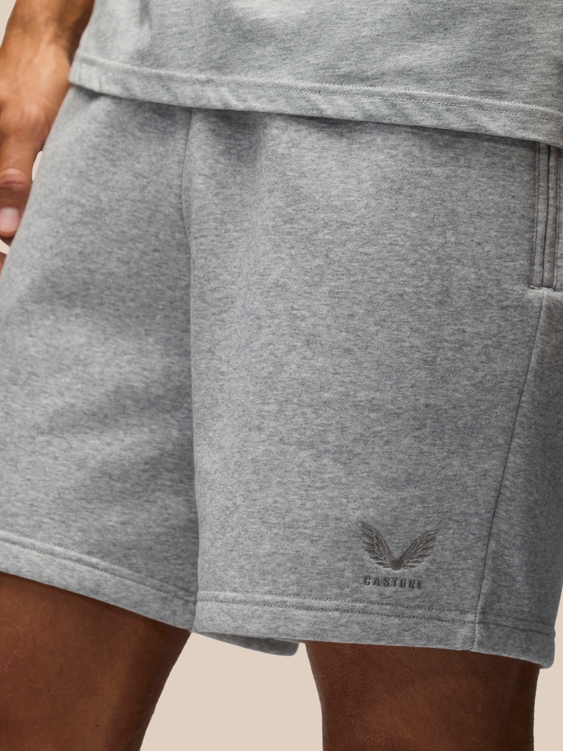 Close-up of a person wearing heather gray shorts with a small dark gray winged logo and the word 'CASTORE' near the lower right leg.