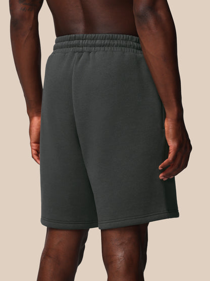 Person wearing dark gray sweat shorts on a beige background