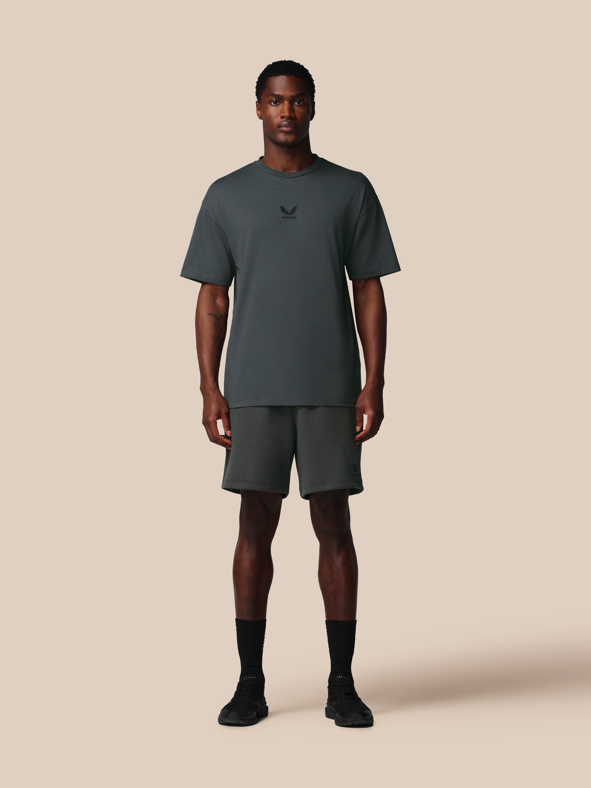 Man wearing a dark gray t-shirt and shorts set on a beige background