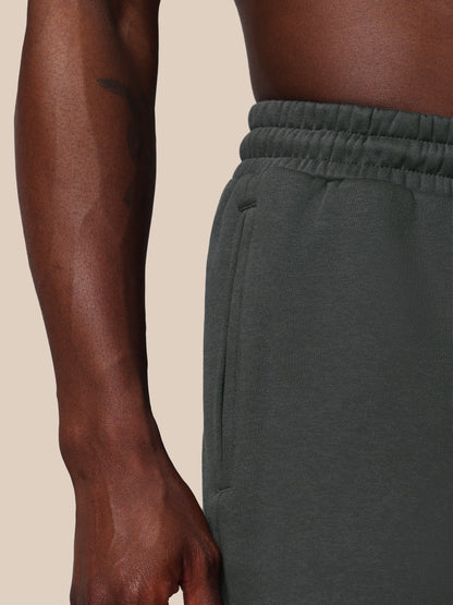 Person wearing dark green sweatpants on a beige background
