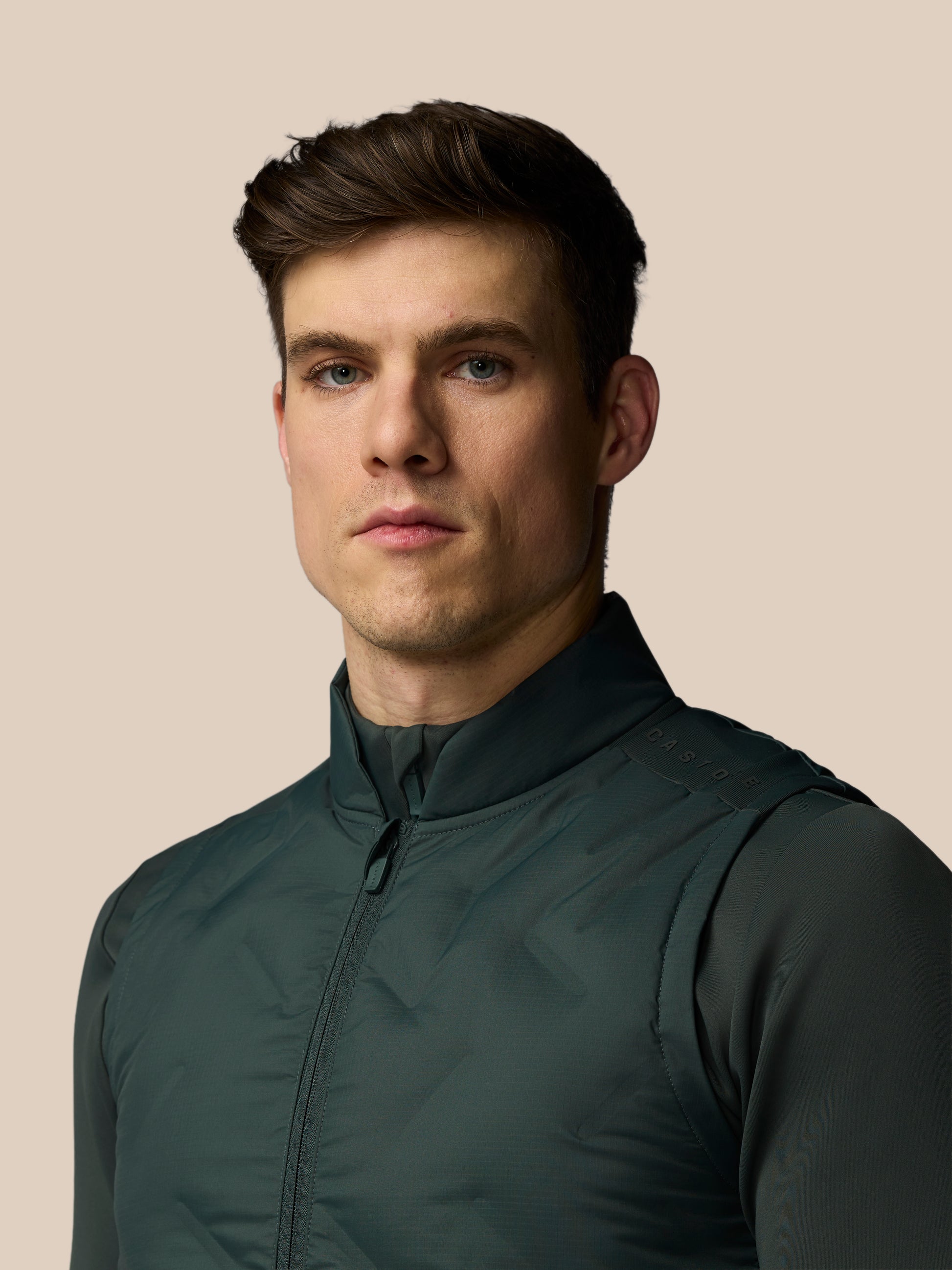 Man wearing a dark green jacket against a beige background