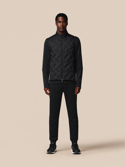 Man wearing a black quilted jacket and pants on a beige background