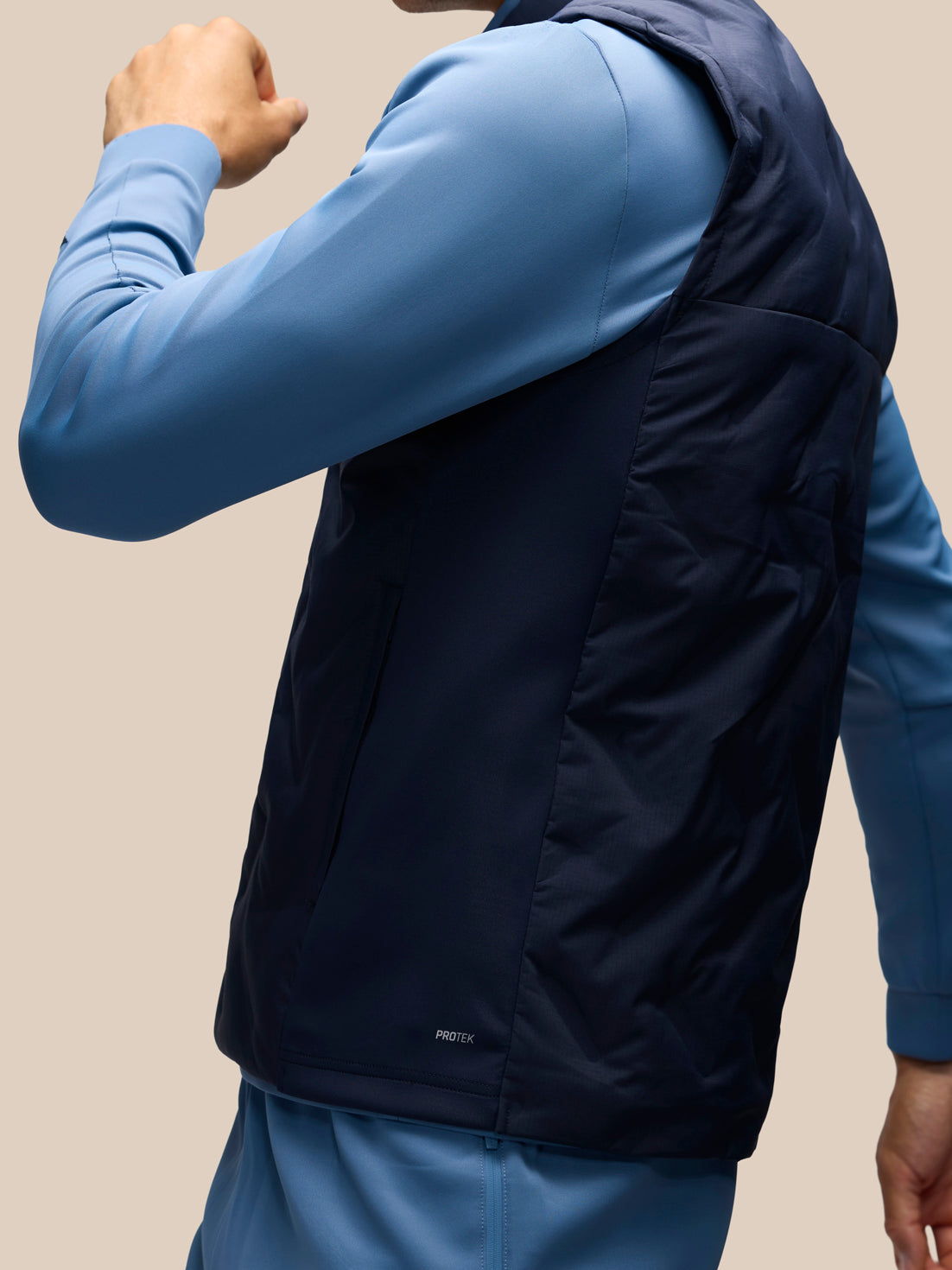 A close-up of a person wearing a dark navy quilted vest over a light blue long-sleeve athletic top, shown from the back against a plain beige background.
