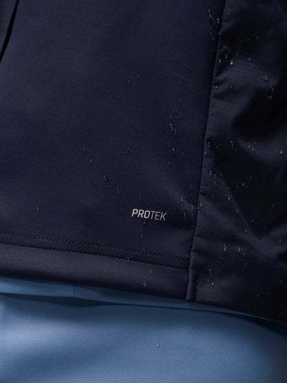 Close-up of a dark navy waterproof jacket fabric with water droplets on the surface and a small 'PROTEK' logo near the hem, set against a blue background.
