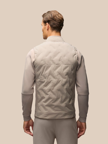 A man shown from the back wearing a light taupe quilted vest over a matching long-sleeve shirt and trousers, set against a solid beige background.