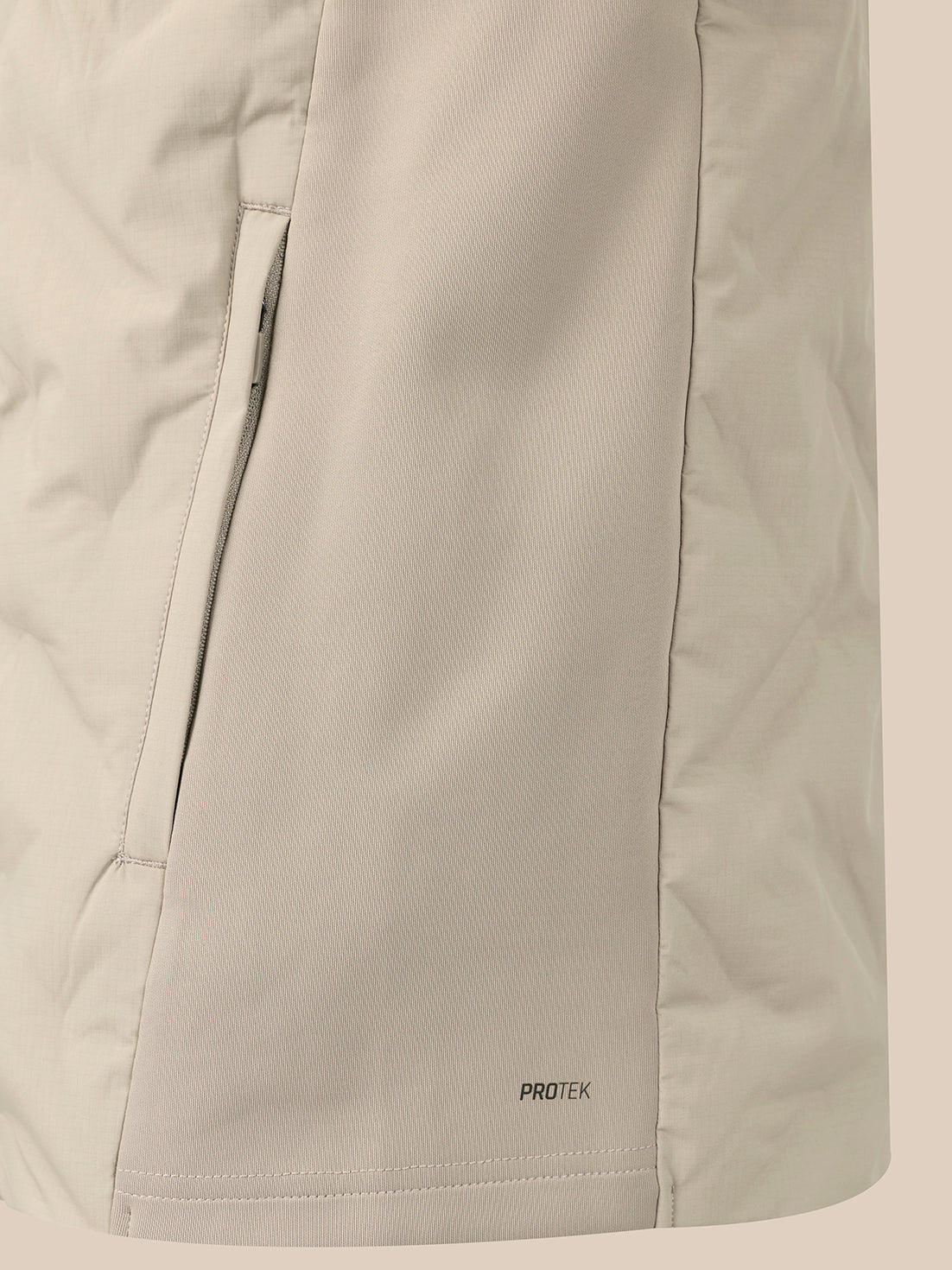 Close-up of a light beige technical jacket fabric with a vertical zip pocket and a small 'PROTEK' logo near the hem.