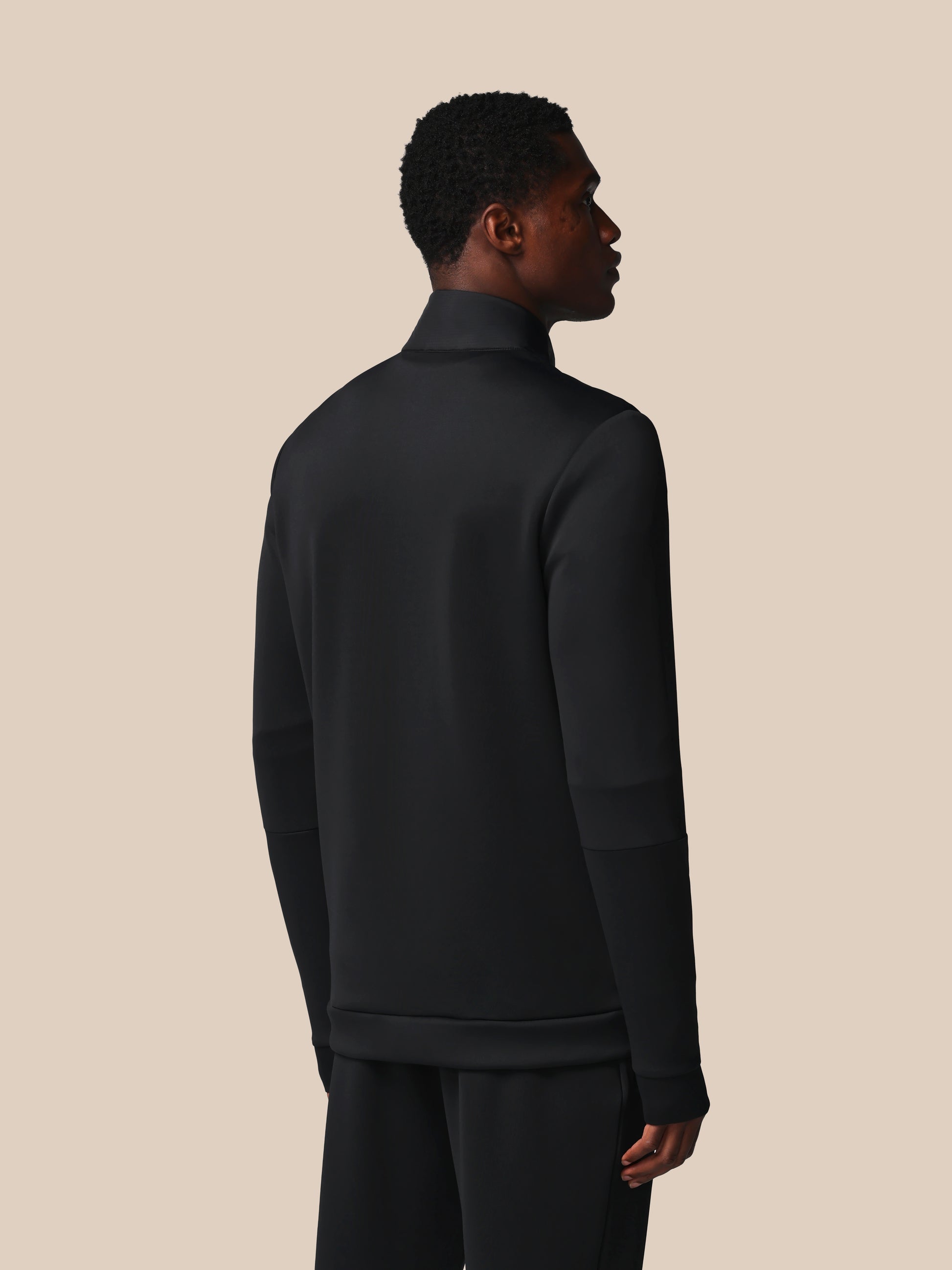 Person wearing a black turtleneck and pants against a beige background