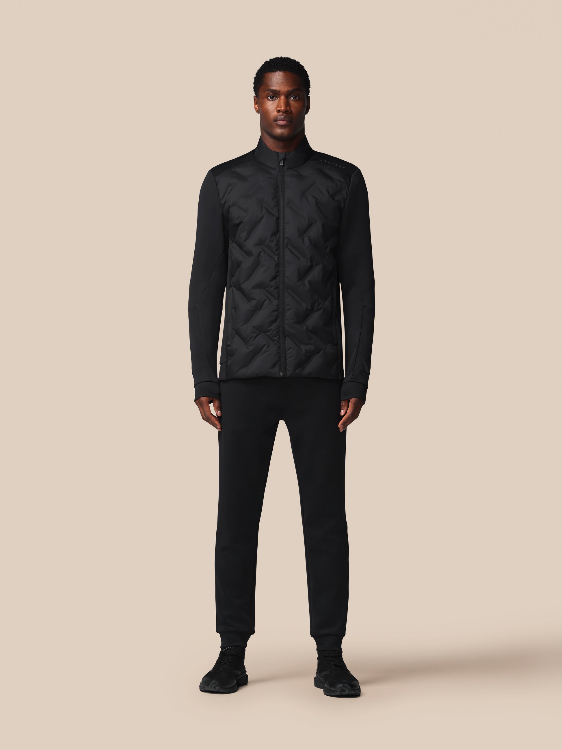 Man wearing a black quilted jacket and pants on a beige background