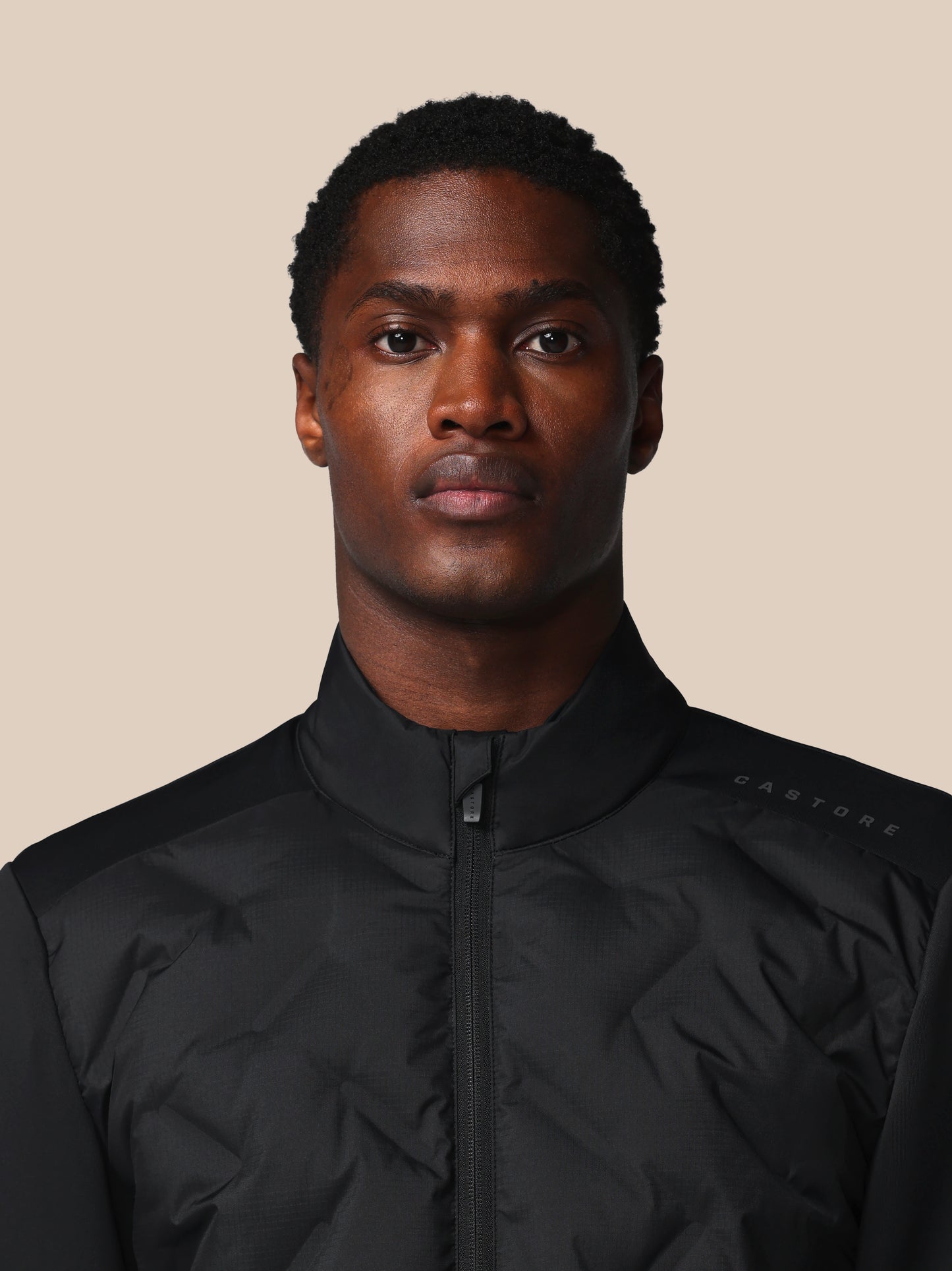 Man wearing a black jacket against a beige background