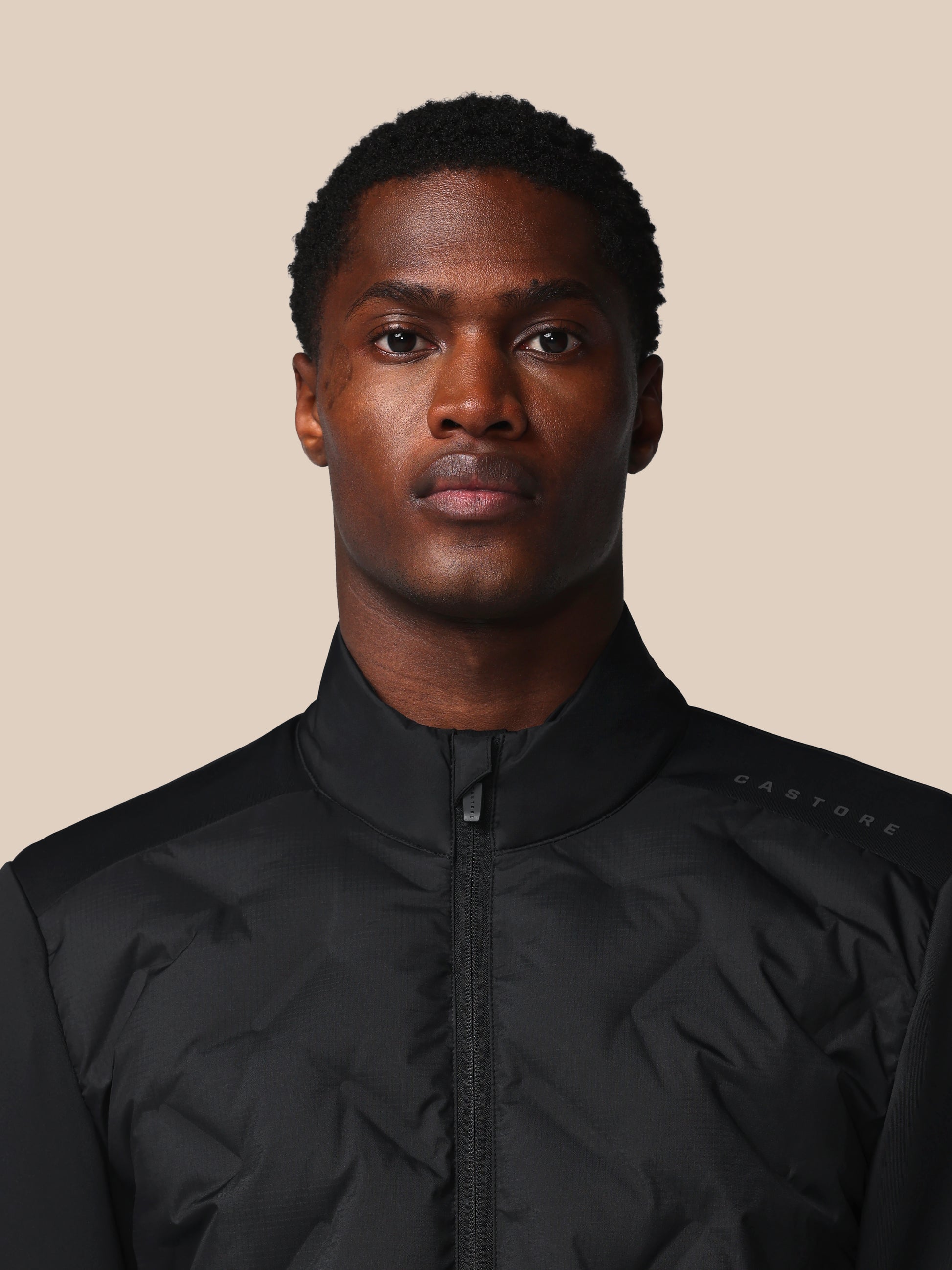 Man wearing a black jacket against a beige background