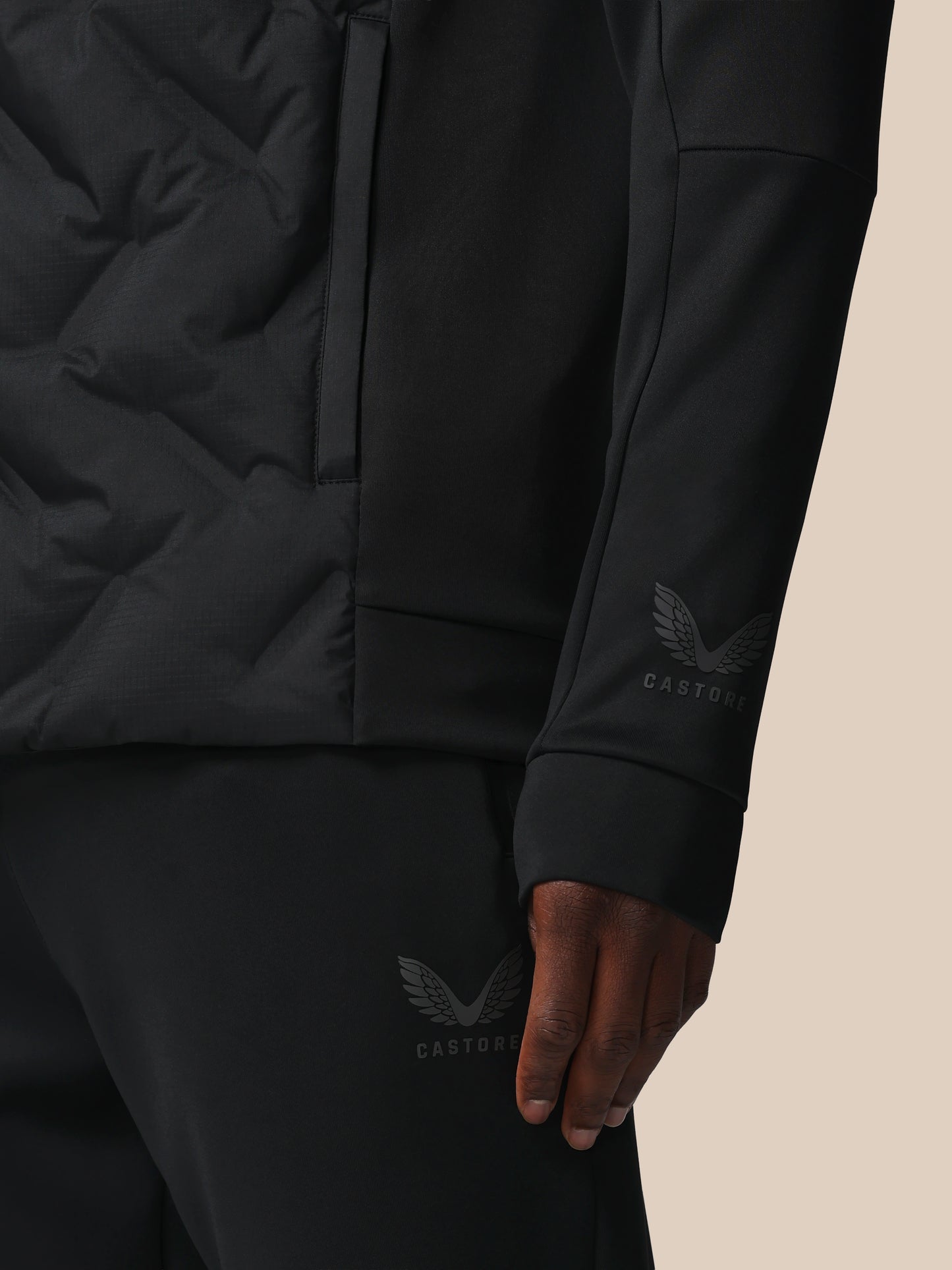 Close-up of a person wearing a black jacket and pants with a brand logo on a beige background