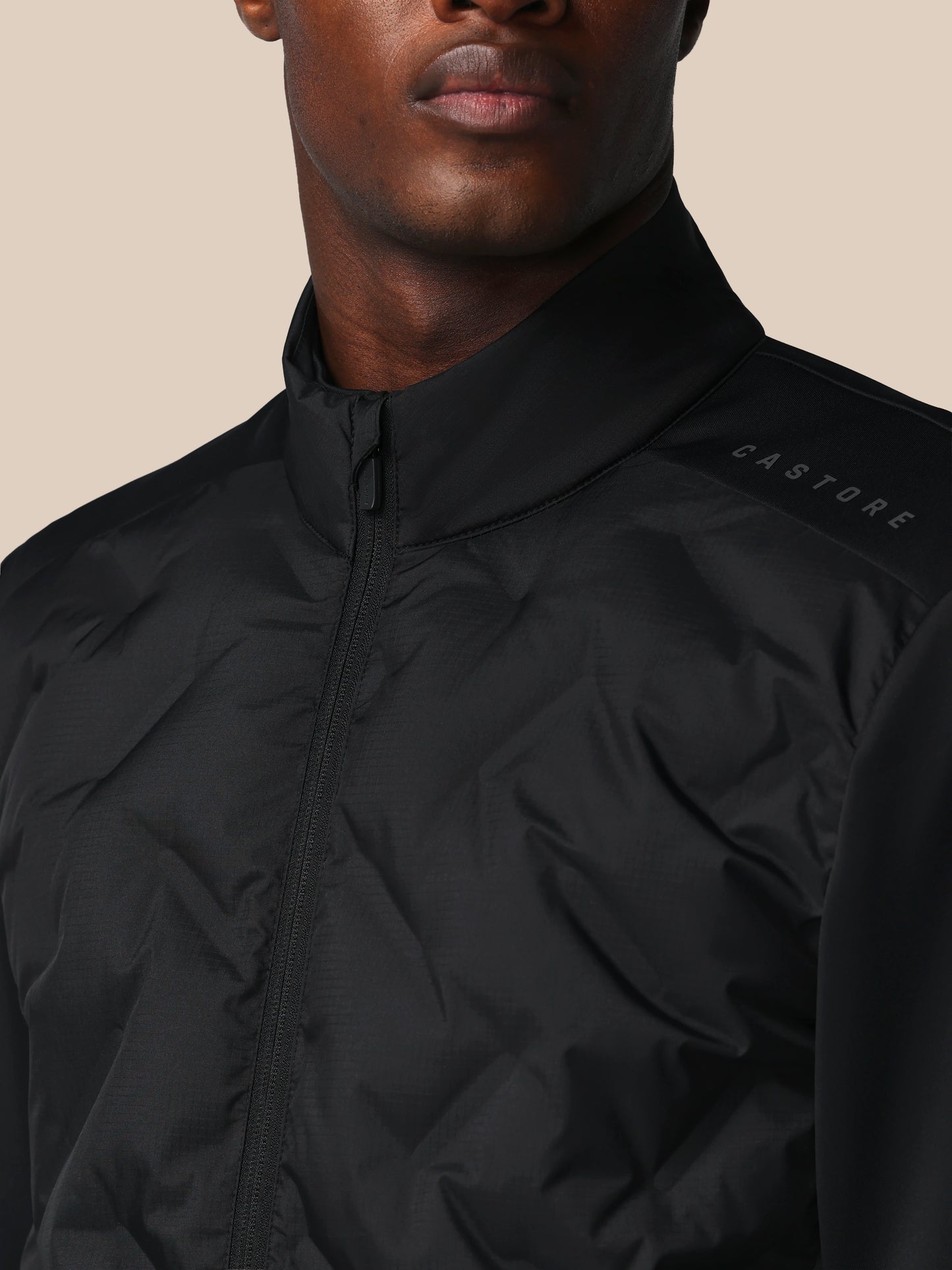 Close-up of a person wearing a black jacket with 'CASTORE' branding on a beige background