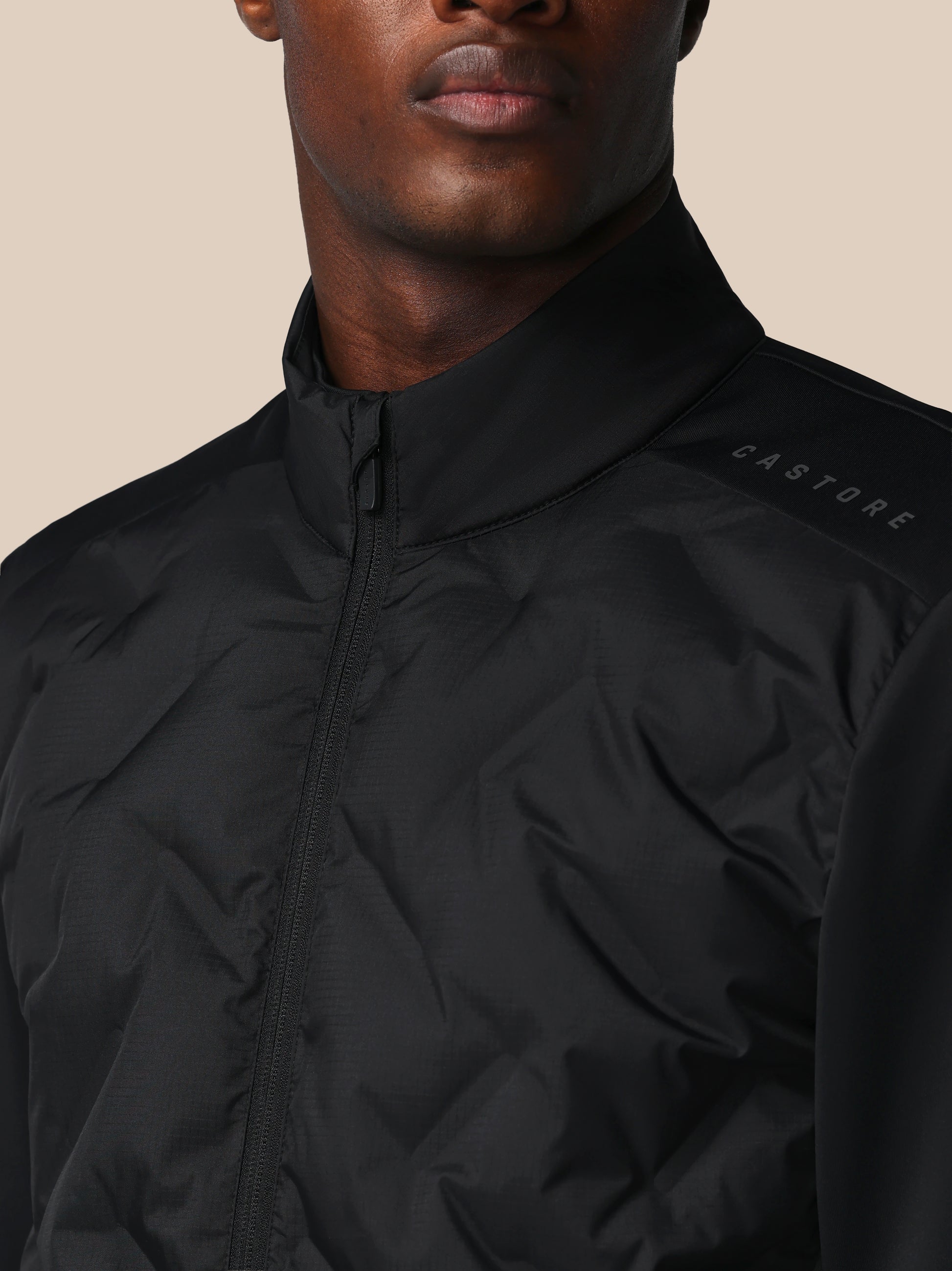 Close-up of a person wearing a black jacket with 'CASTORE' branding on a beige background