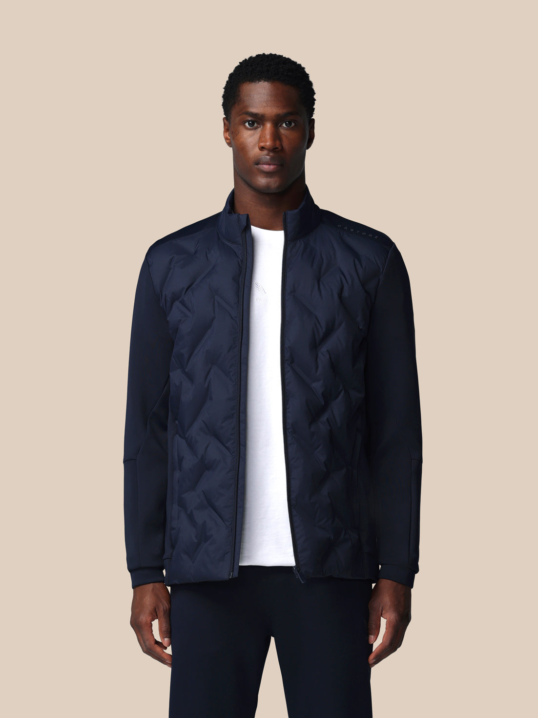 Man wearing a navy quilted jacket over a white shirt on a beige background
