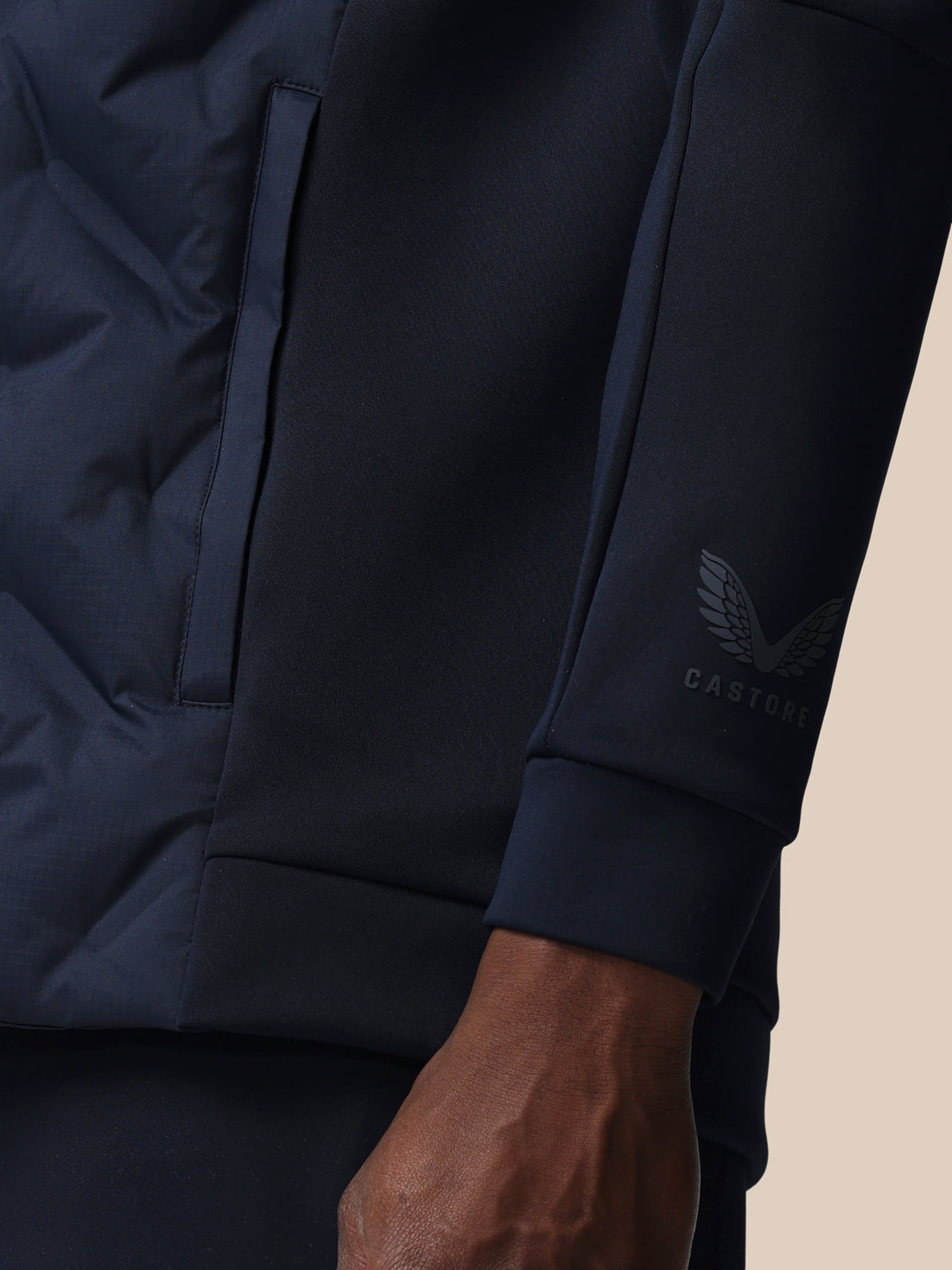 Close-up of a navy blue jacket with a brand logo on the sleeve against a beige background