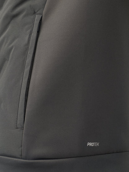 Close-up of a dark gray technical jacket fabric with a vertical zip pocket and a small white PROTEK logo near the bottom.