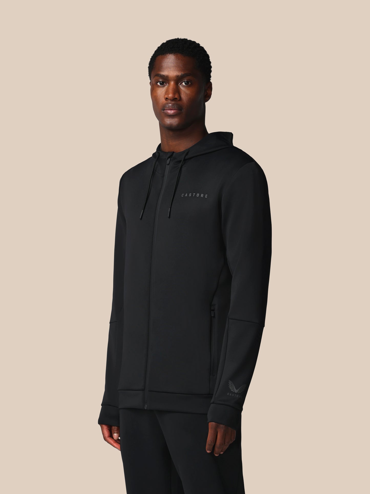 Man wearing a black hoodie with a brand logo on a beige background