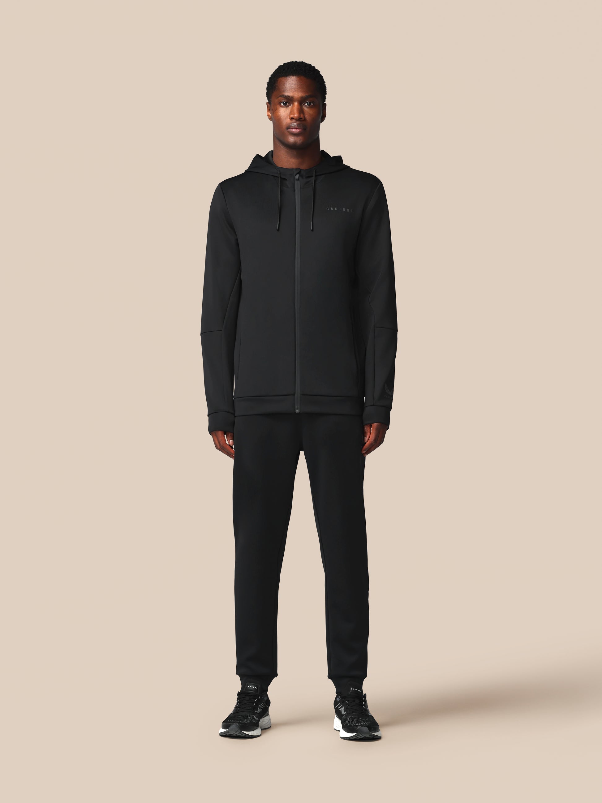 Person wearing a black hoodie and pants on a beige background