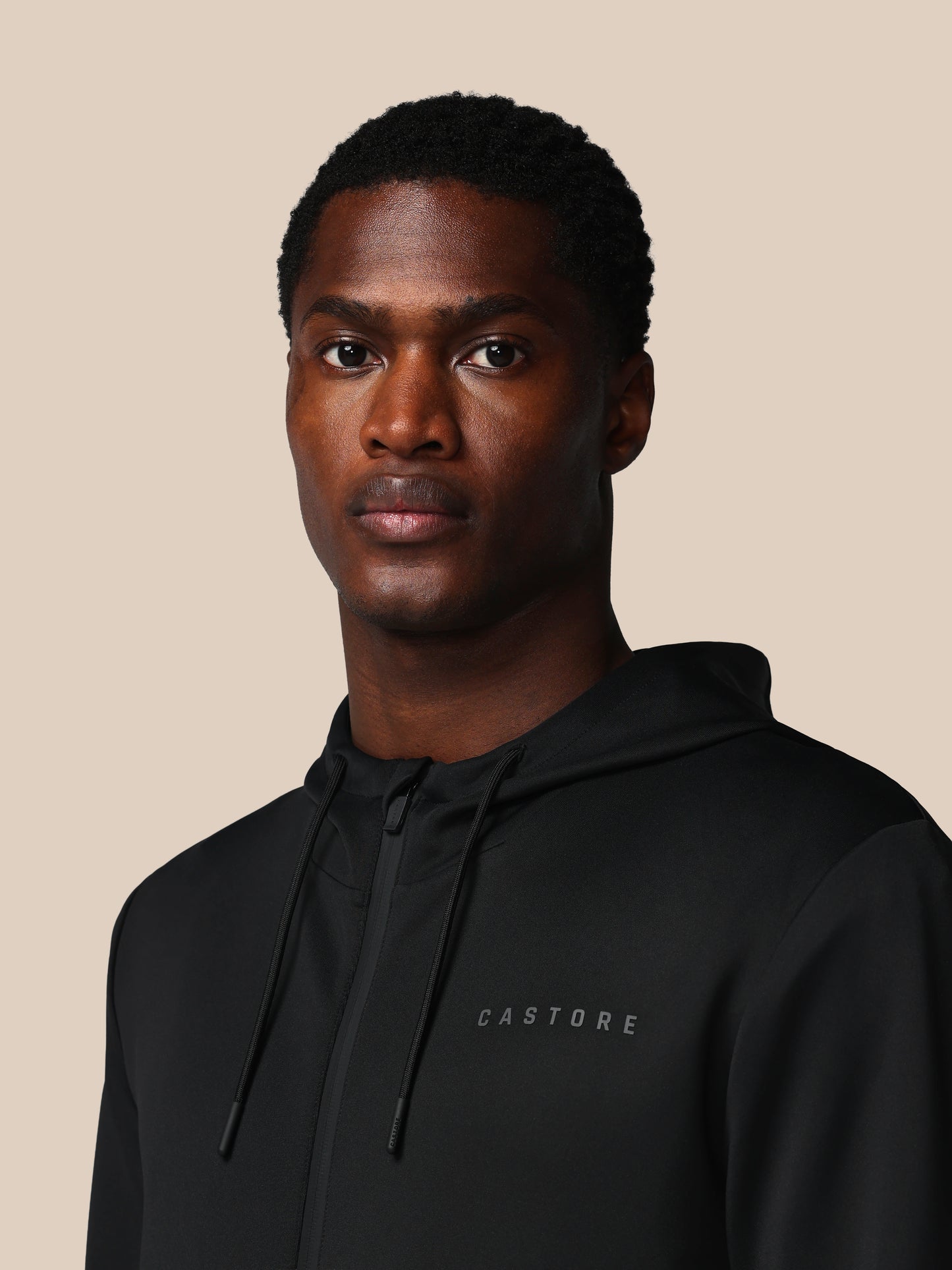Man wearing a black hoodie with 'CASTORE' branding on a beige background