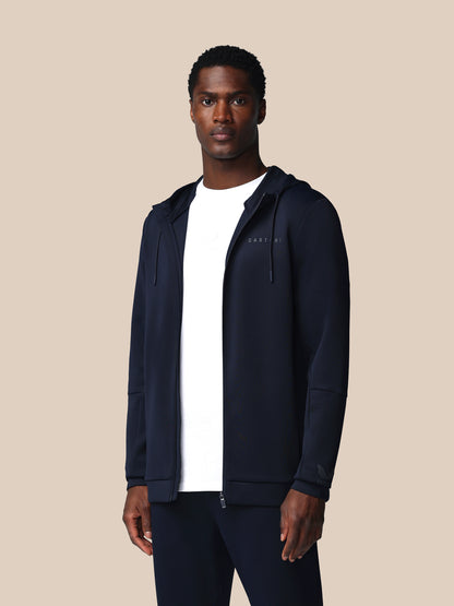Man wearing a navy blue hoodie over a white shirt on a beige background