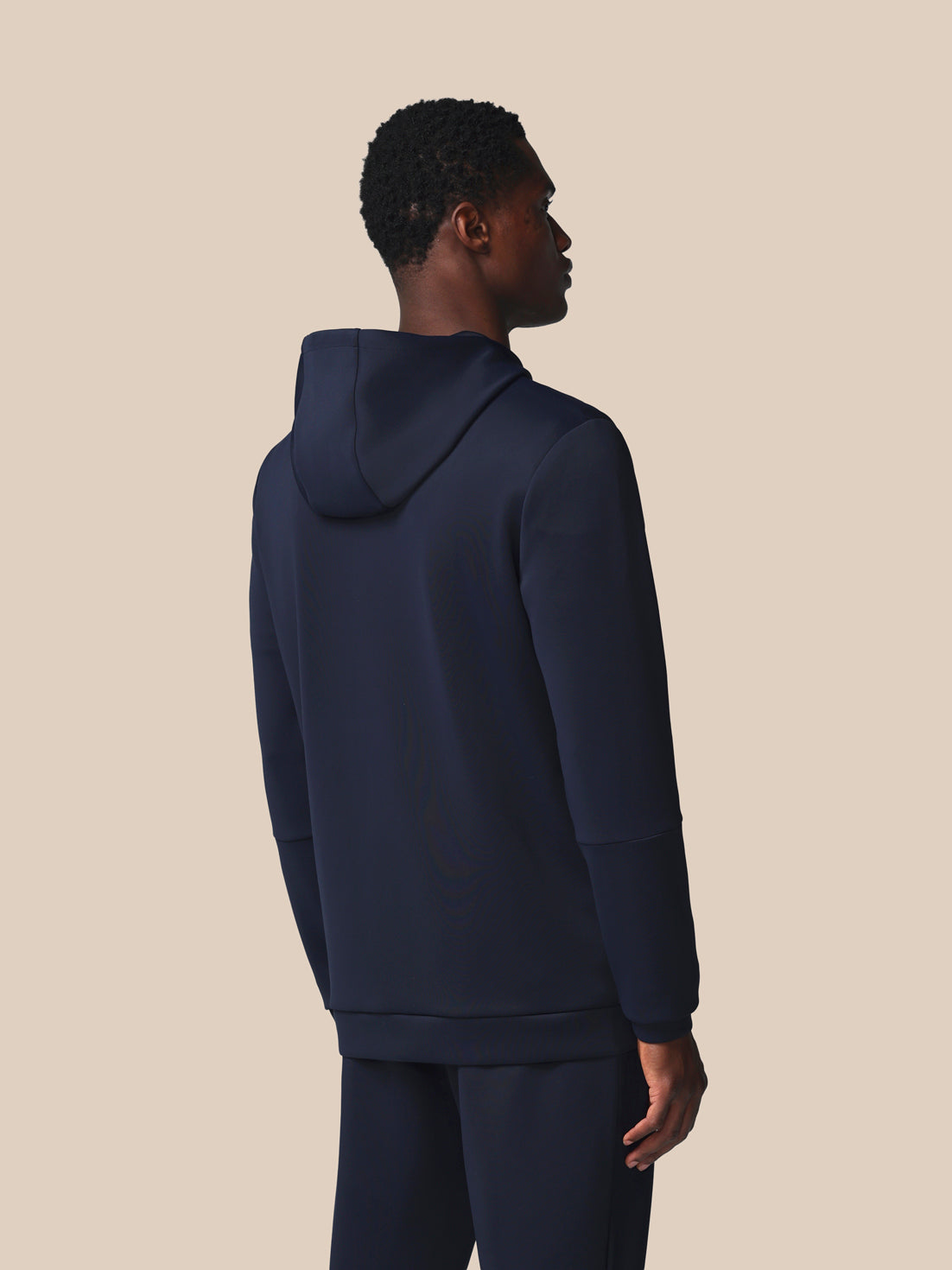 Person wearing a navy blue hoodie and pants on a beige background