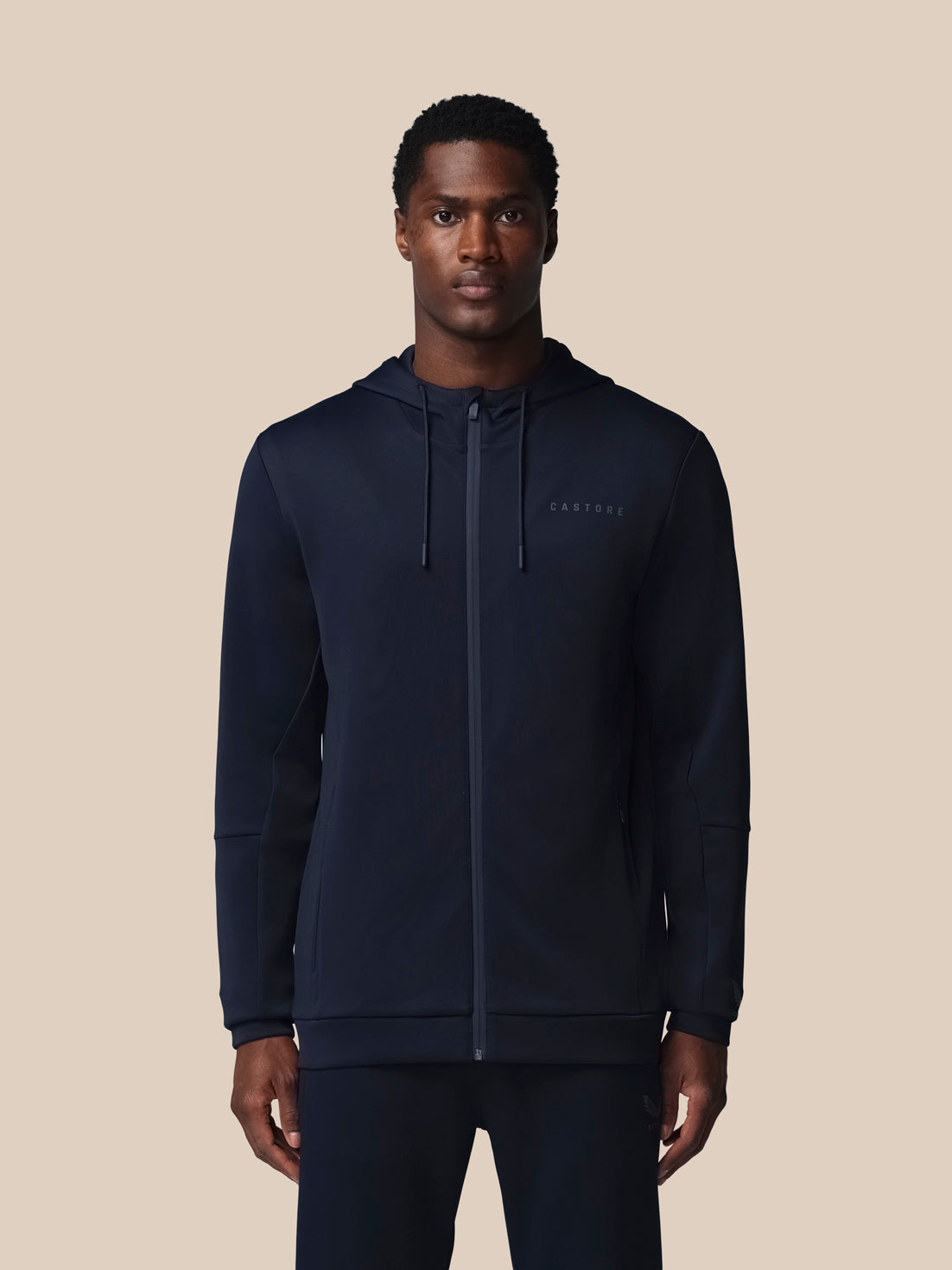 Man wearing a navy hoodie with a brand logo on a beige background