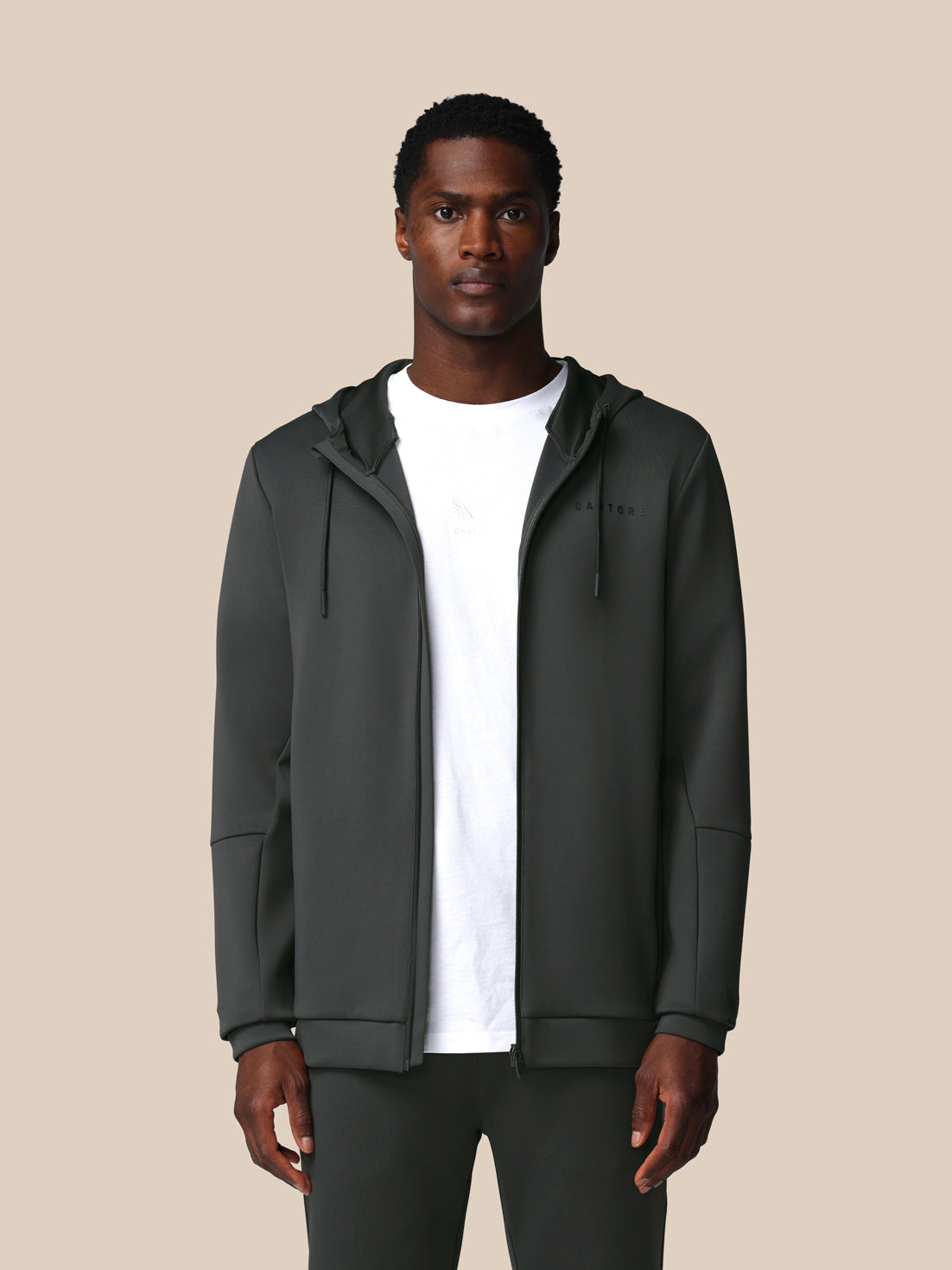 Man wearing a dark gray hoodie over a white shirt on a beige background