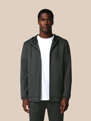 Man wearing a dark gray hoodie over a white shirt on a beige background