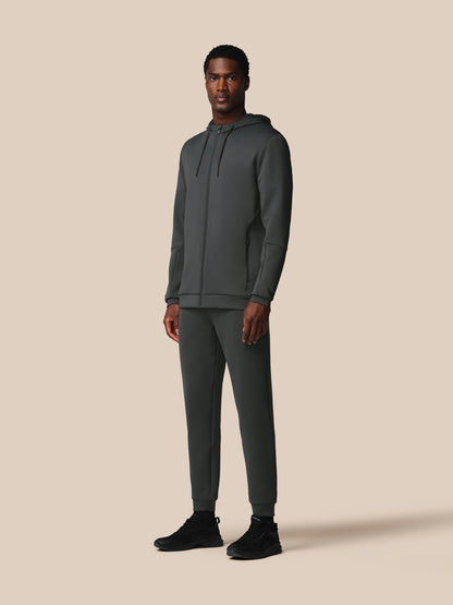 Man wearing a dark gray hoodie and pants on a beige background