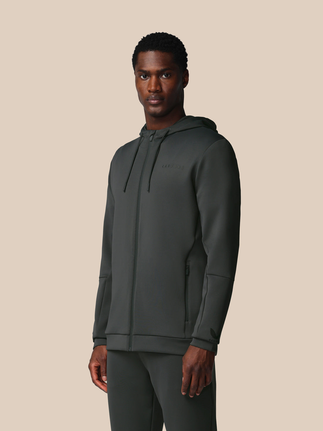 Man wearing a dark gray hoodie and pants on a beige background