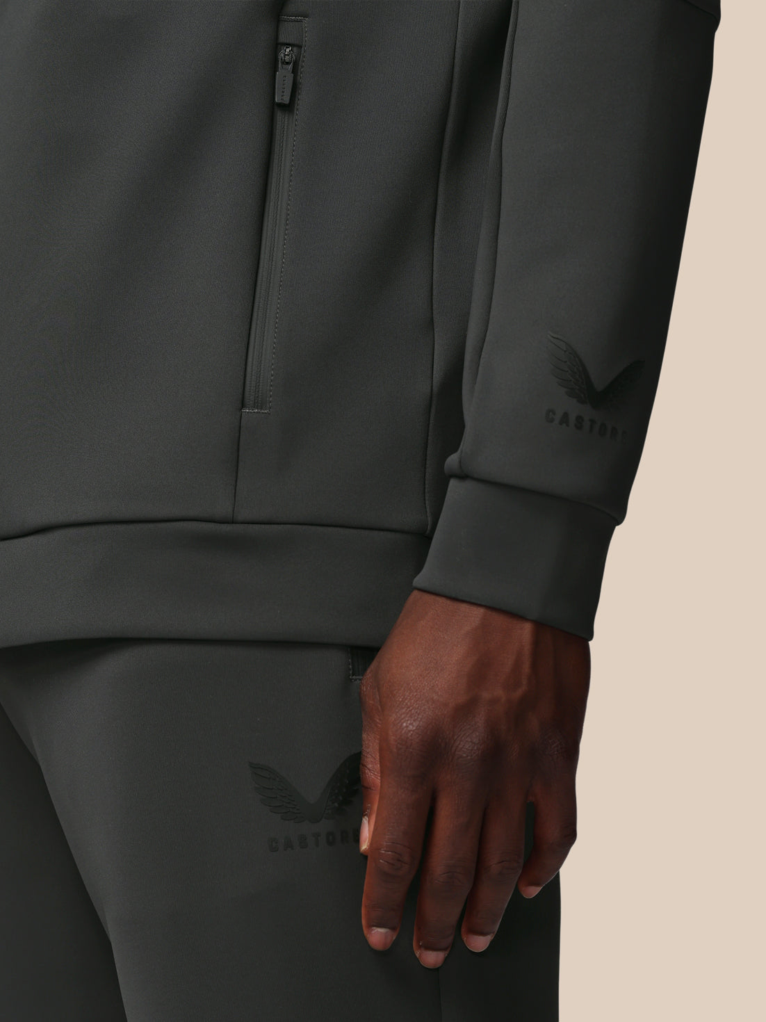Person wearing a dark gray tracksuit with brand logo on beige background