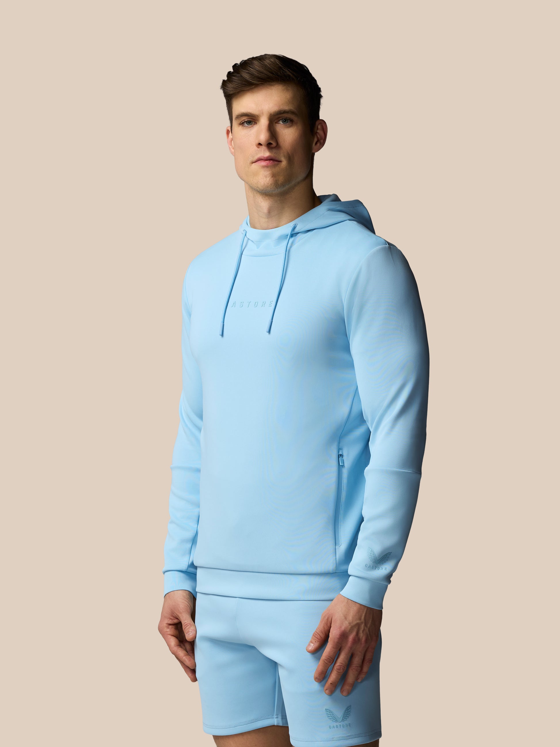 Man wearing a light blue hoodie and shorts set on a beige background