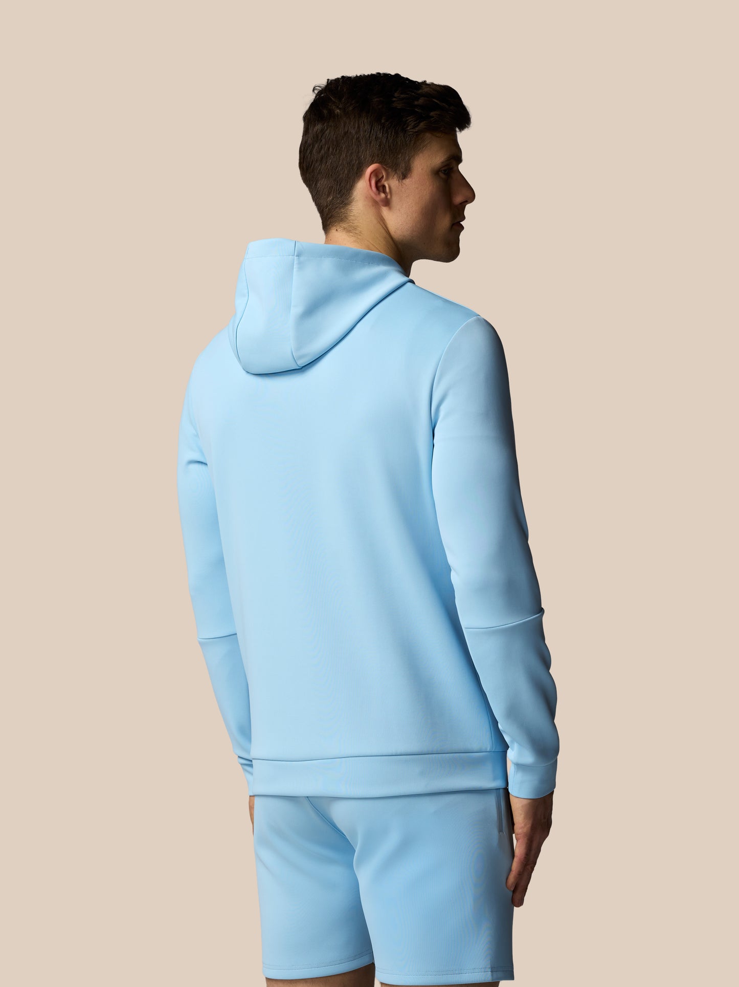 Person wearing a light blue hoodie and shorts set on a beige background