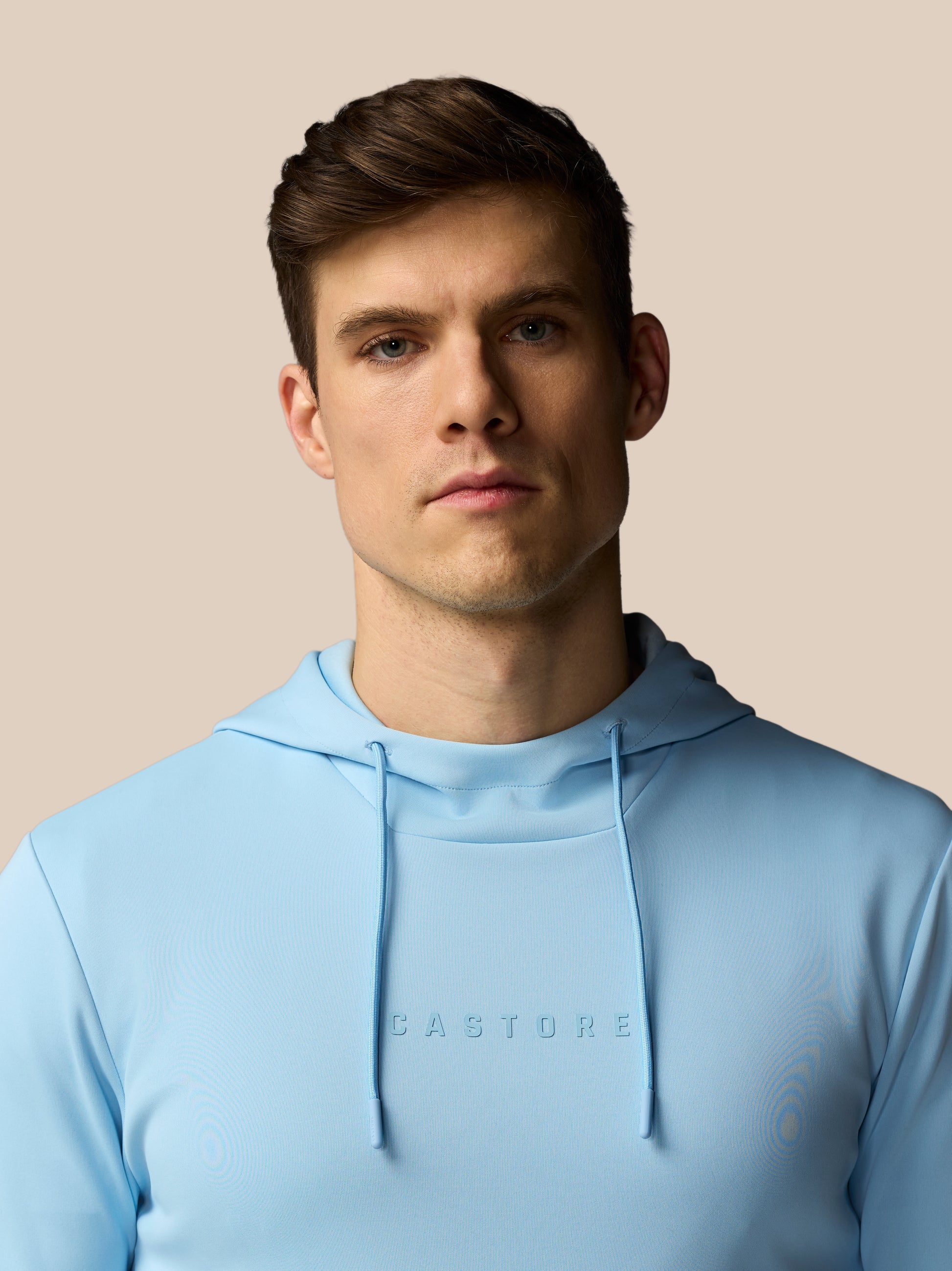 Man wearing a light blue hoodie with 'CASTORE' branding against a beige background