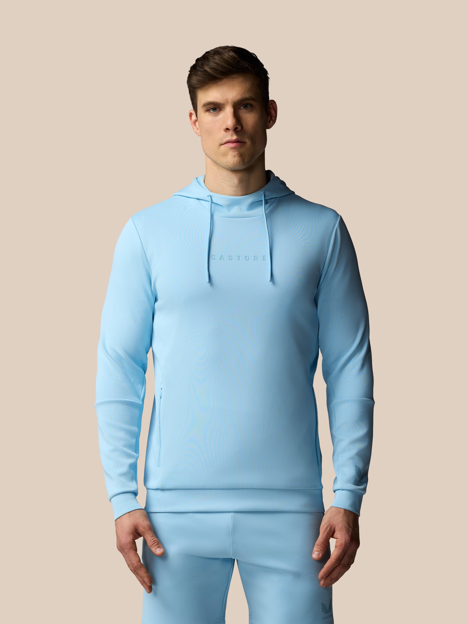 Man wearing a light blue hoodie and pants on a beige background