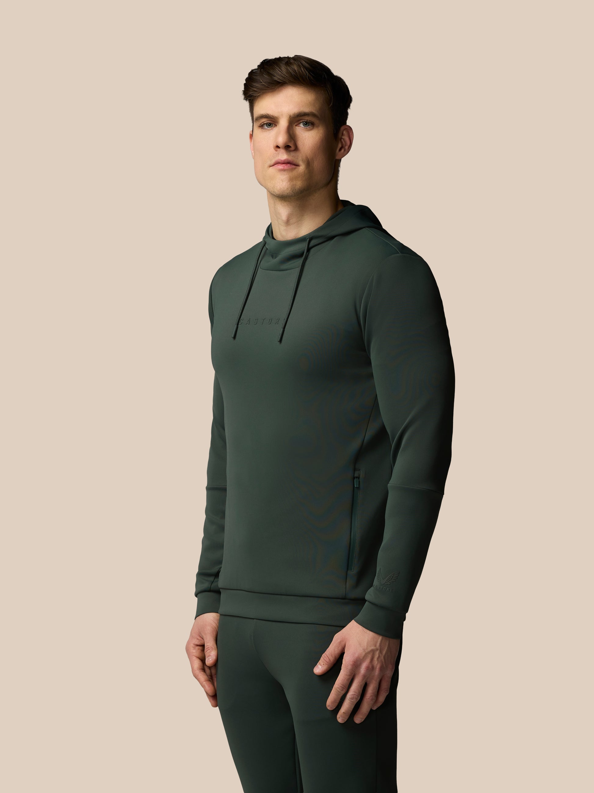 Man wearing a dark green hoodie and pants on a beige background