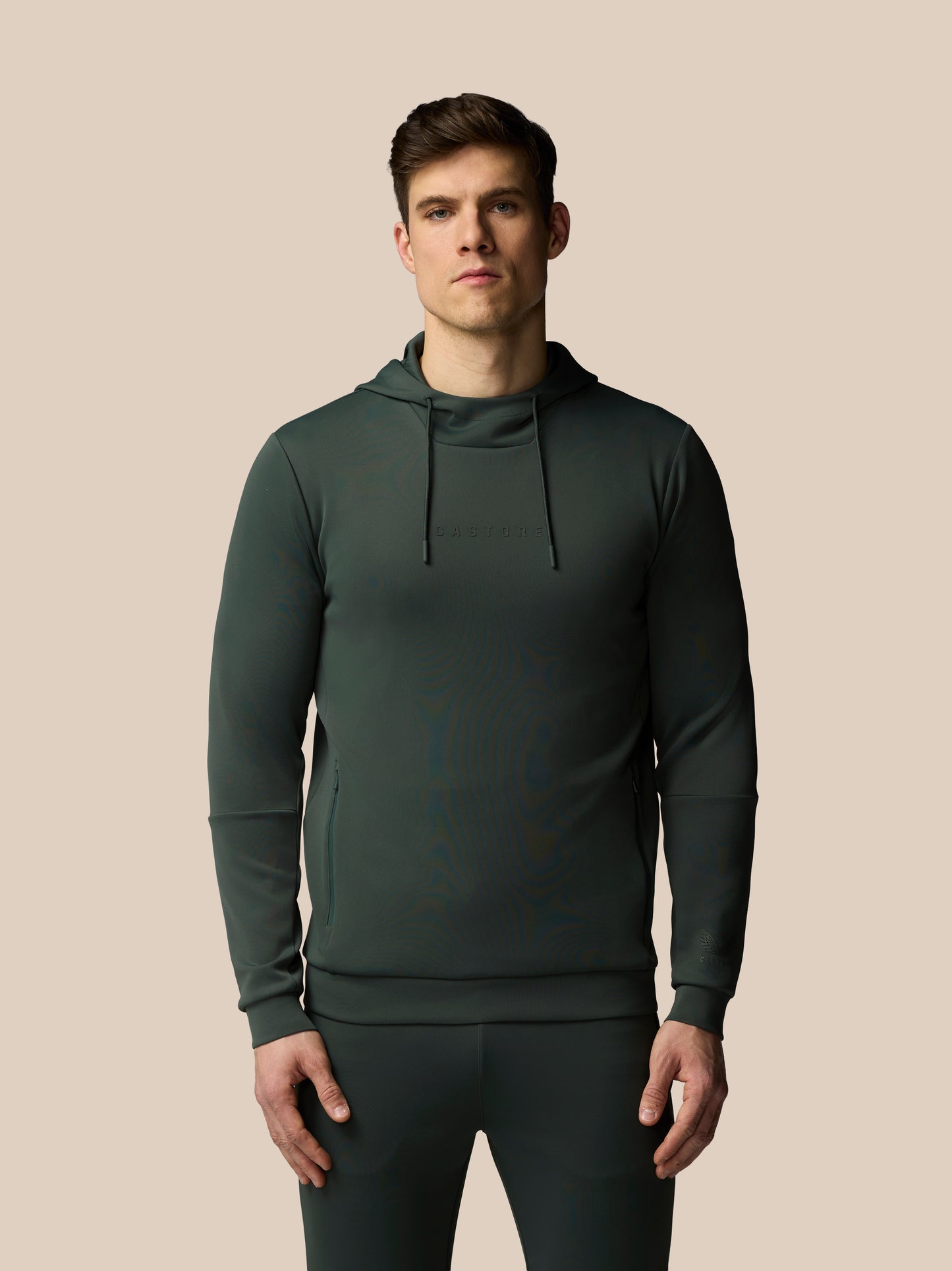 Man wearing a dark green hoodie and pants on a beige background
