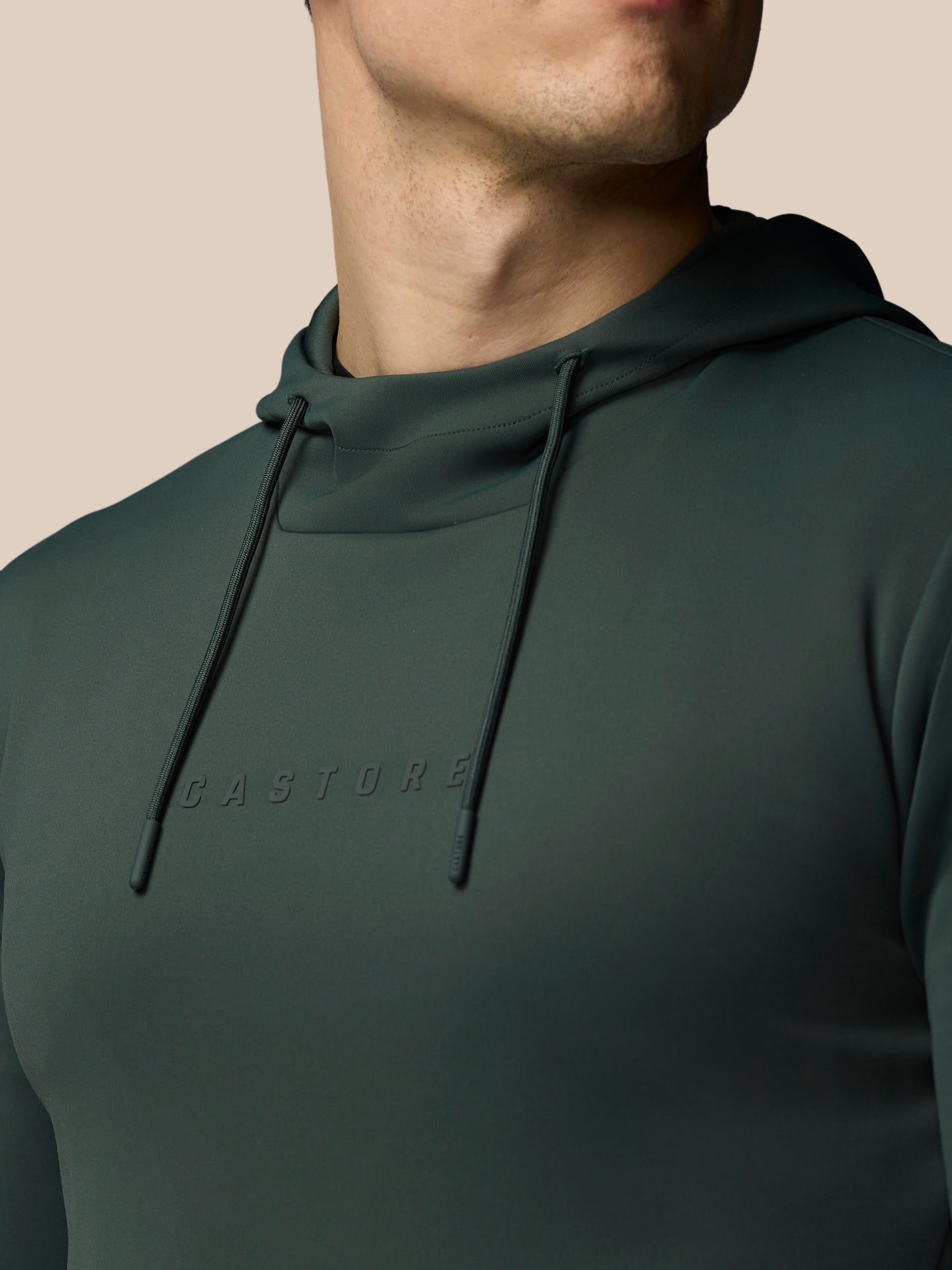 Person wearing a dark green hoodie with 'CASTORE' branding on a beige background