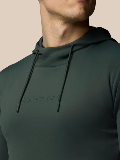Person wearing a dark green hoodie with 'CASTORE' branding on a beige background