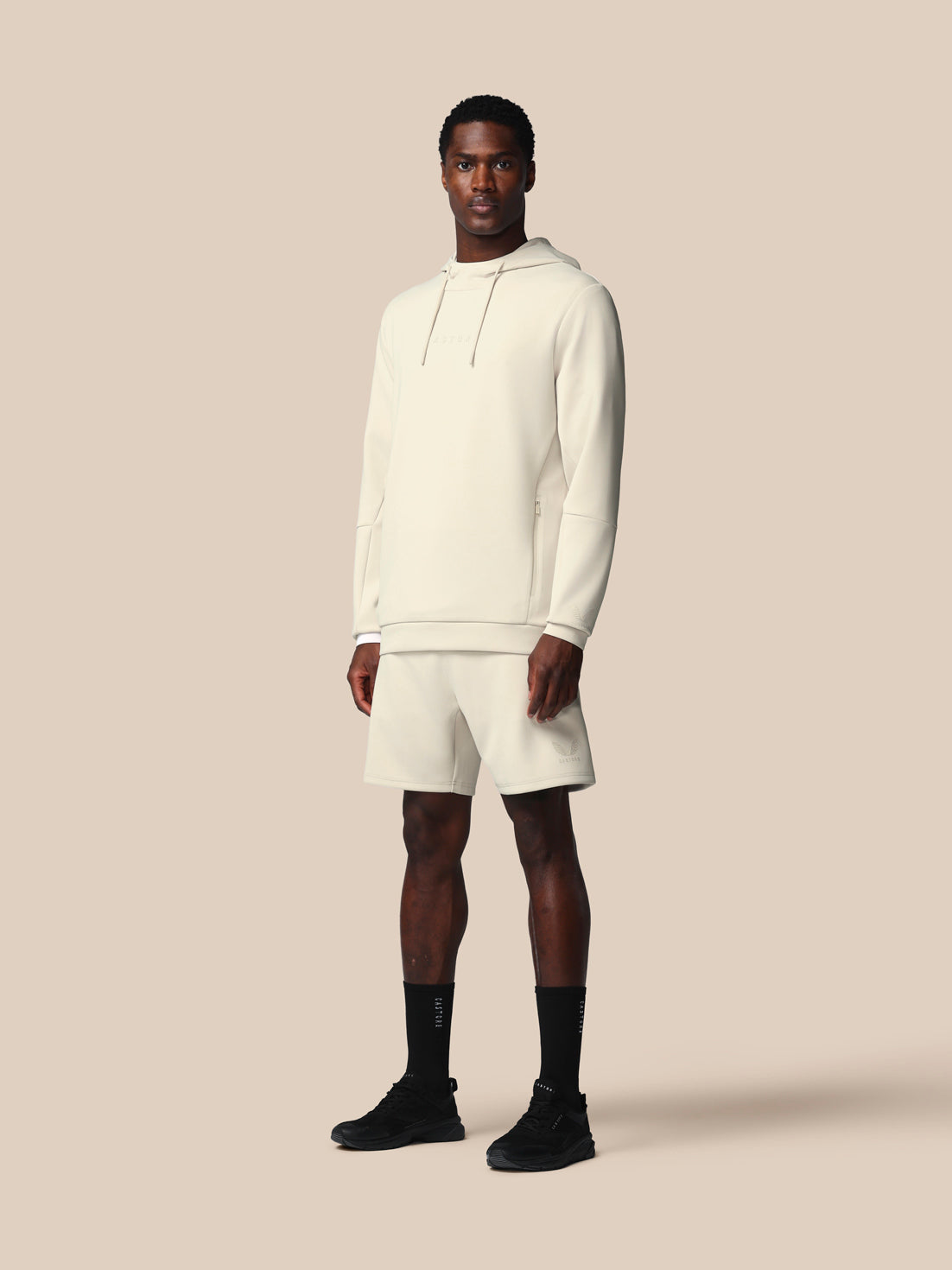 Man wearing a white hoodie and shorts set on a beige background