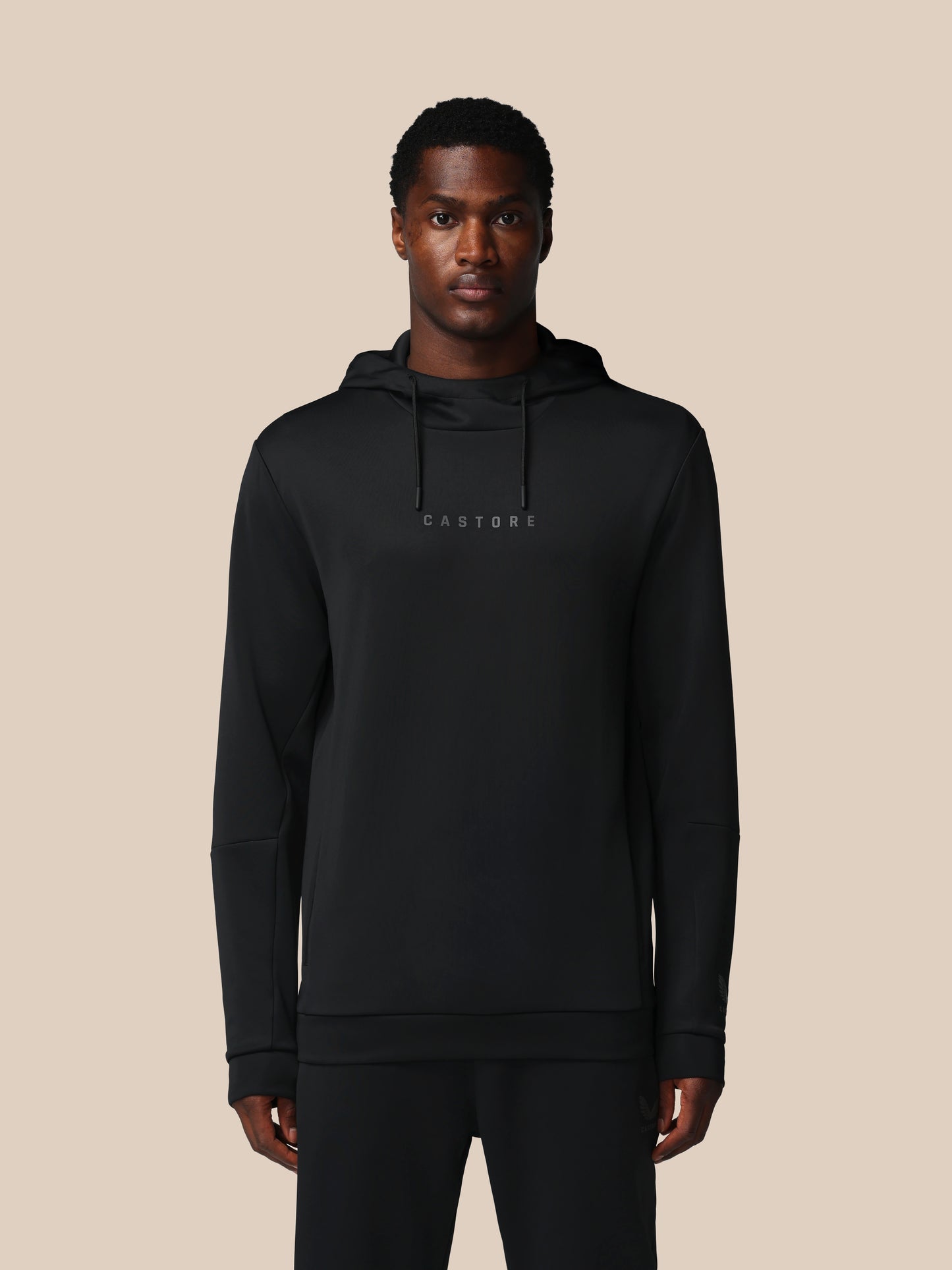 Man wearing a black hoodie with 'CASTORE' branding on a beige background