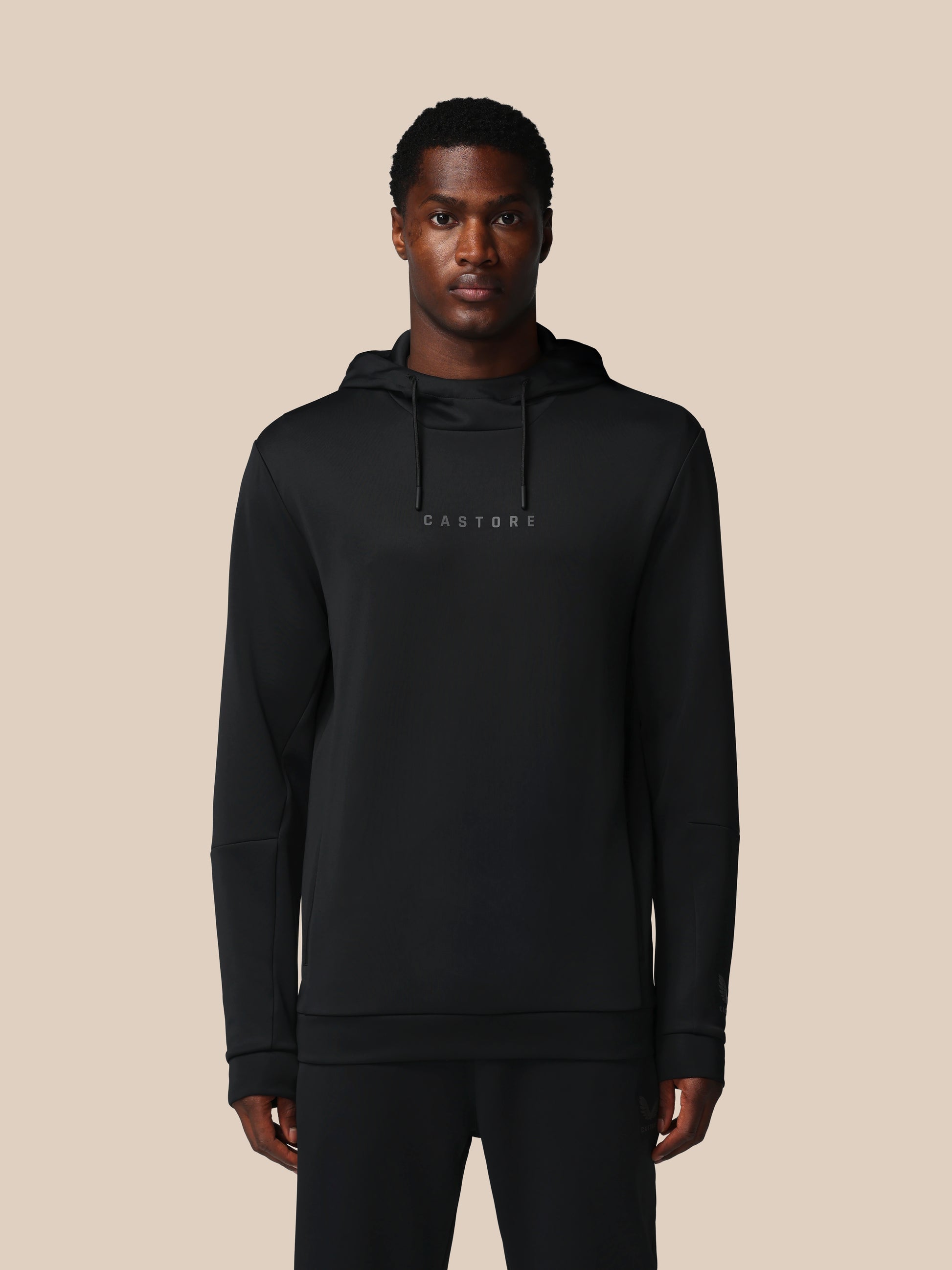 Man wearing a black hoodie with 'CASTORE' branding on a beige background