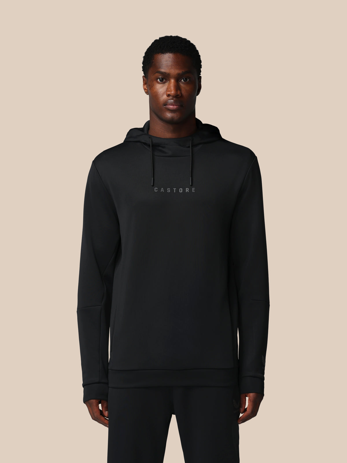 Man wearing a black hoodie with 'CASTORE' branding on a beige background