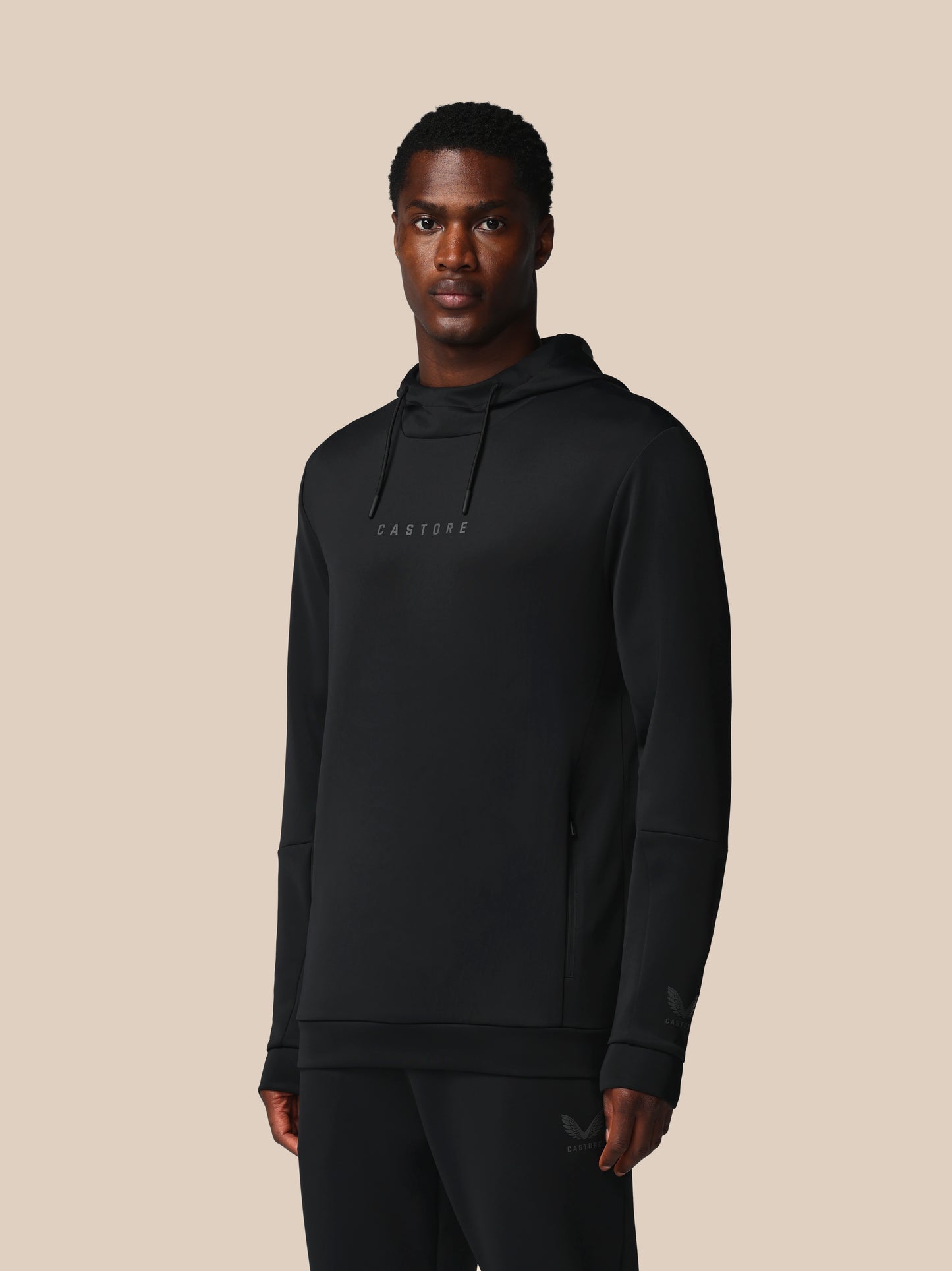 Man wearing a black hoodie with a brand logo on a beige background