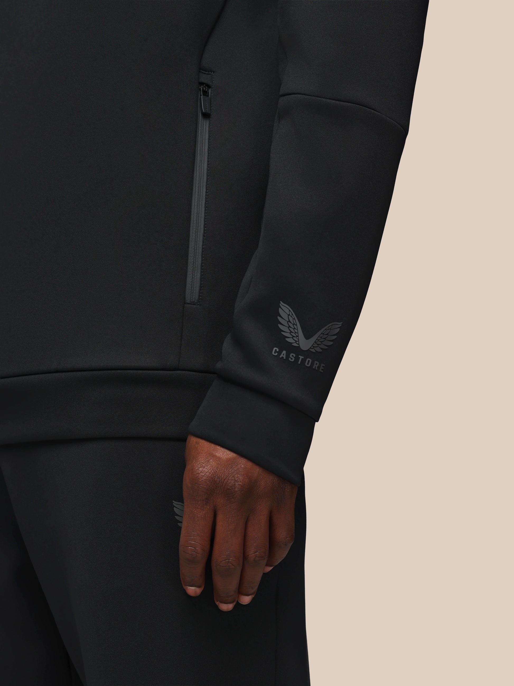 Black athletic jacket with brand logo on sleeve against a beige background