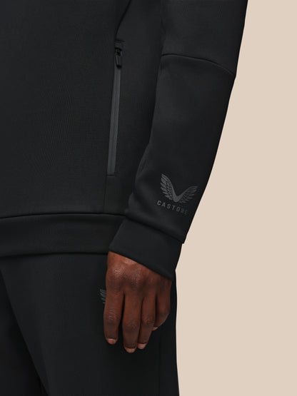 Black athletic jacket with brand logo on sleeve against a beige background