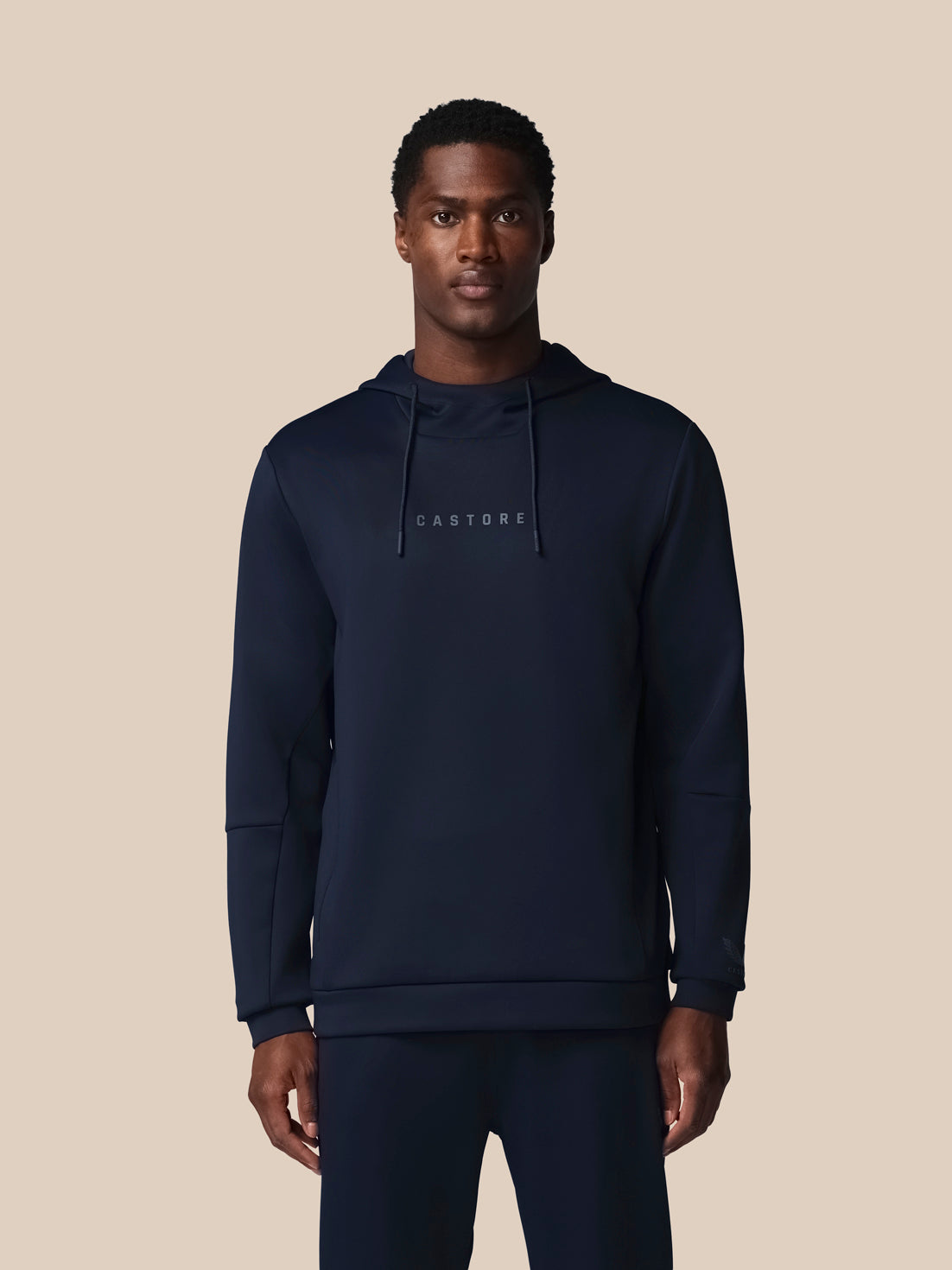Man wearing a navy hoodie with 'CASTORE' branding on a beige background