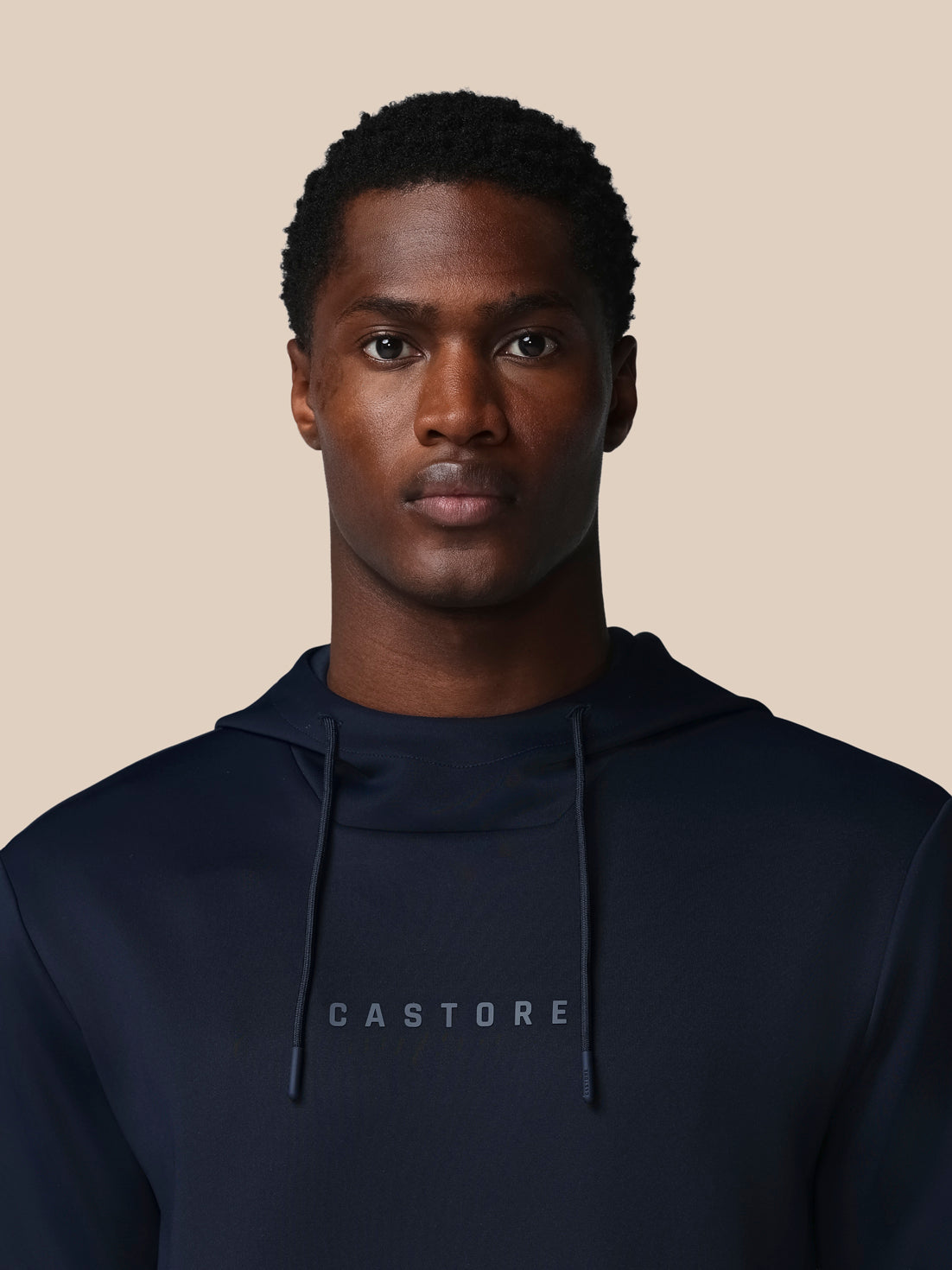 Man wearing a black hoodie with 'CASTORE' logo against a beige background