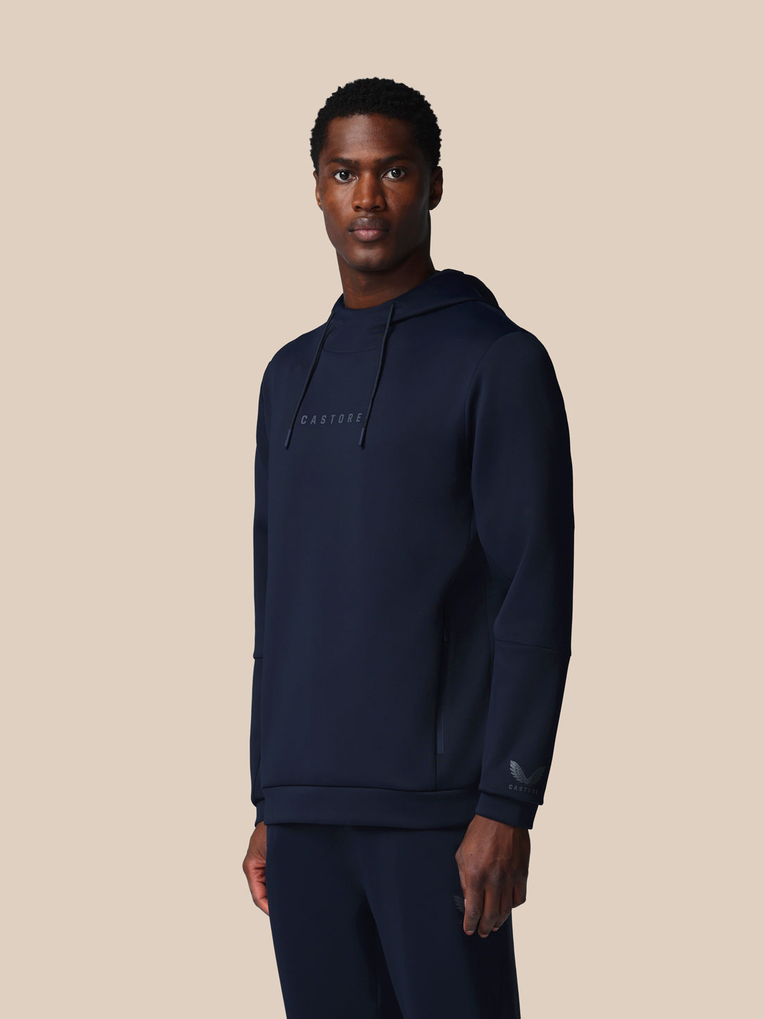 Man wearing a navy hoodie with a brand logo on a beige background